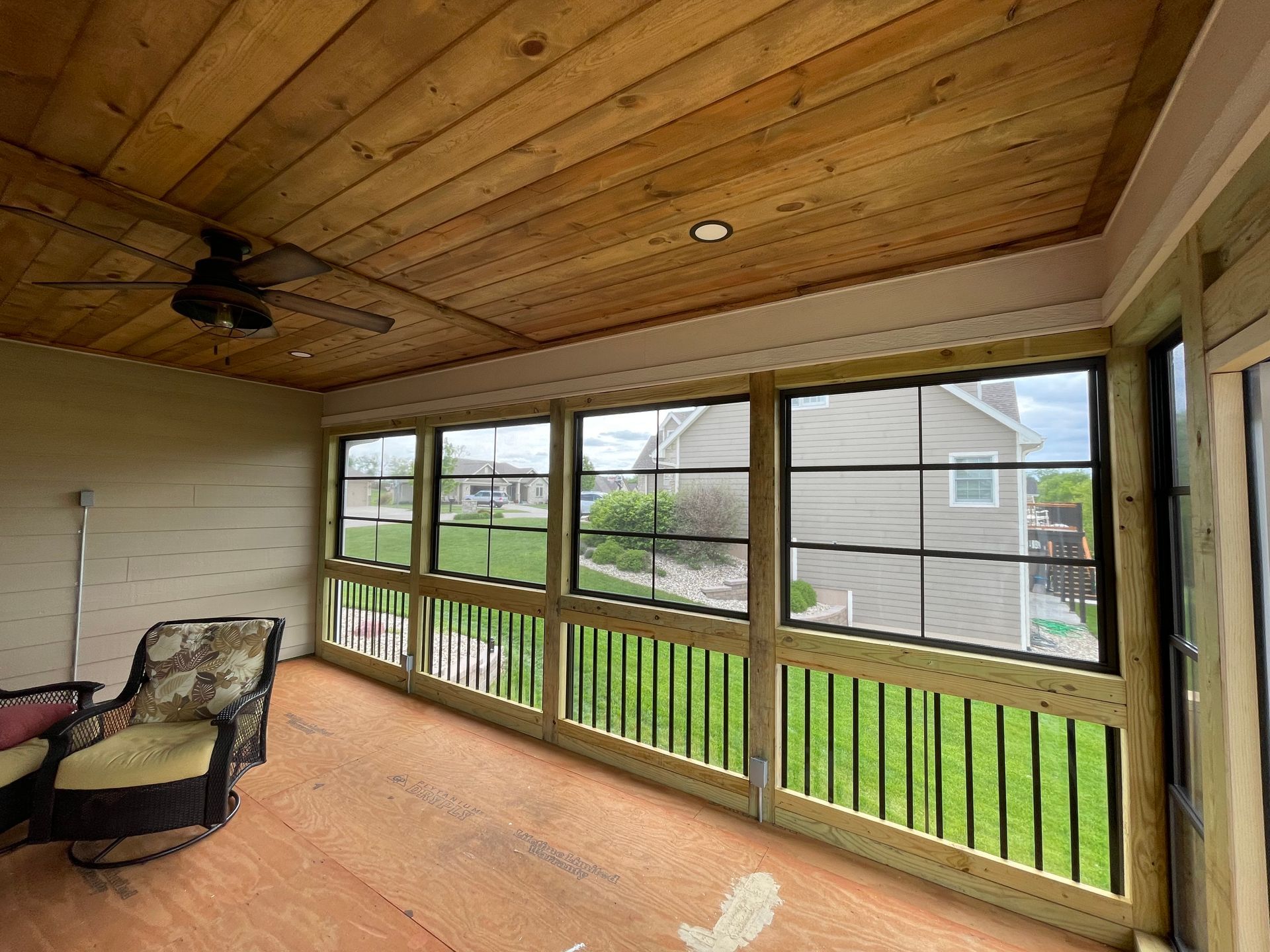 Enclosed porch with wood ceiling and floors, large windows, and black railing.
