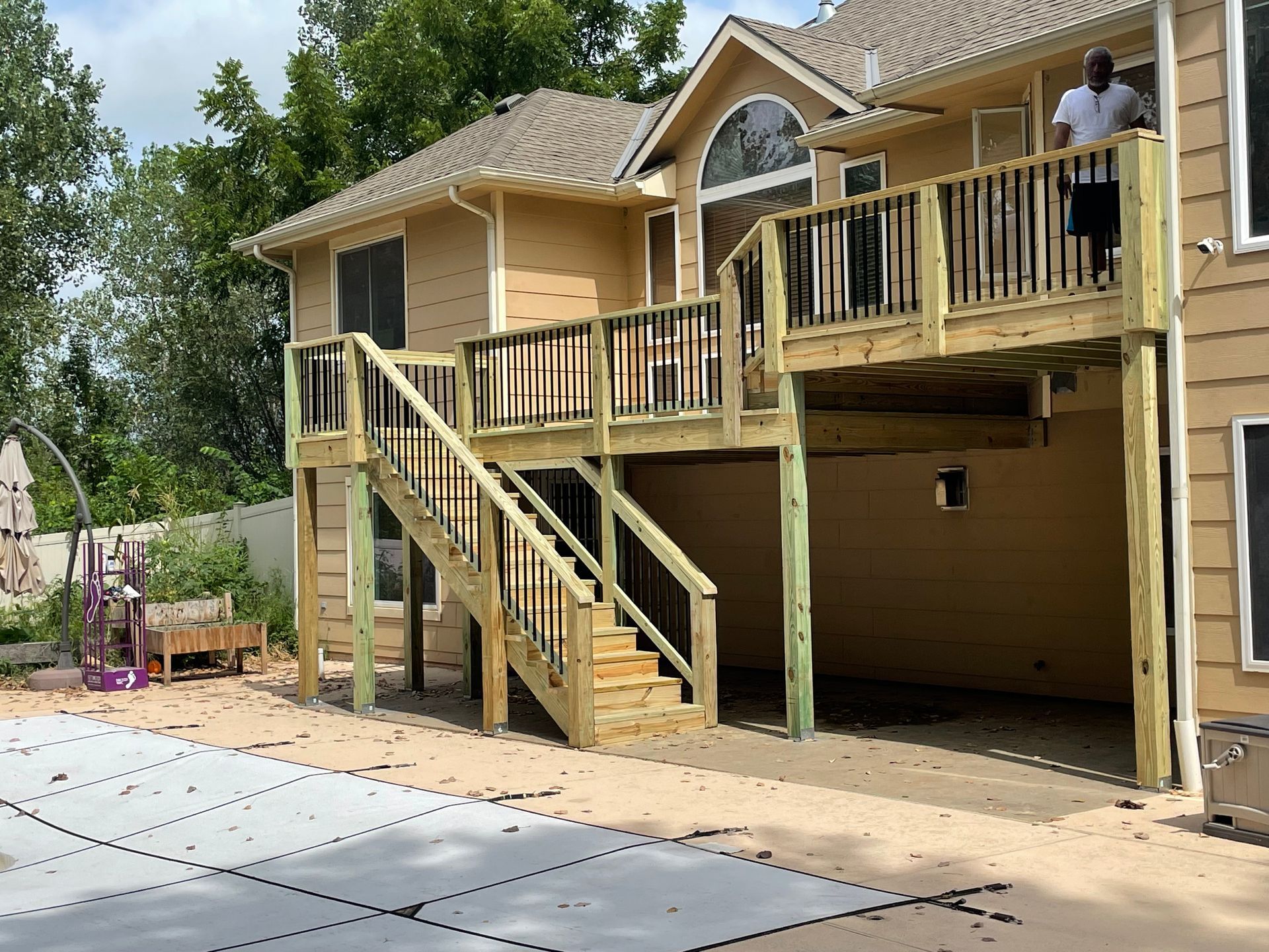Two-story wooden deck attached to a light yellow house. A person stands on the upper level.