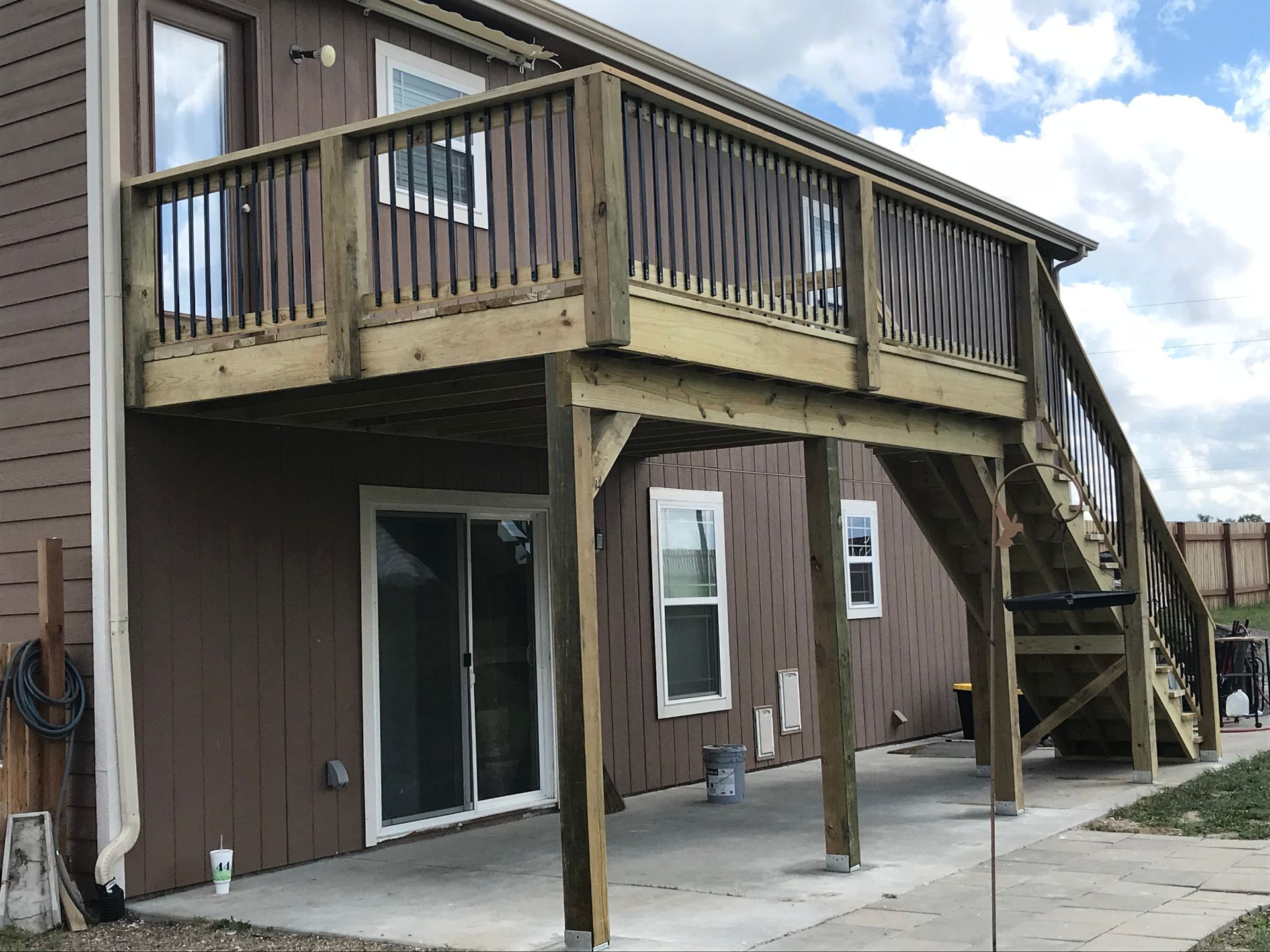 Wooden deck with stairs attached to a brown house with a sliding glass door and a concrete patio.