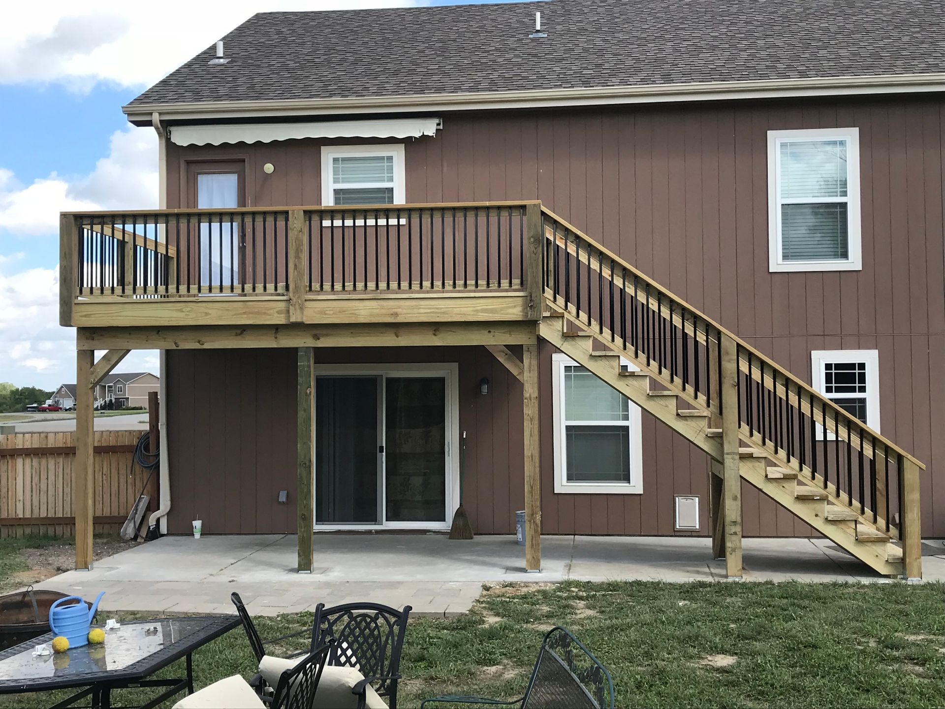 Wooden deck and stairs on the back of a brown house; a sliding glass door and windows are visible.