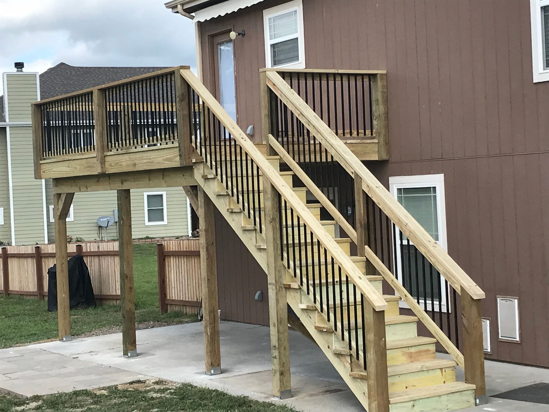 Wooden deck and stairs on a brown house with black railings and light-colored steps.