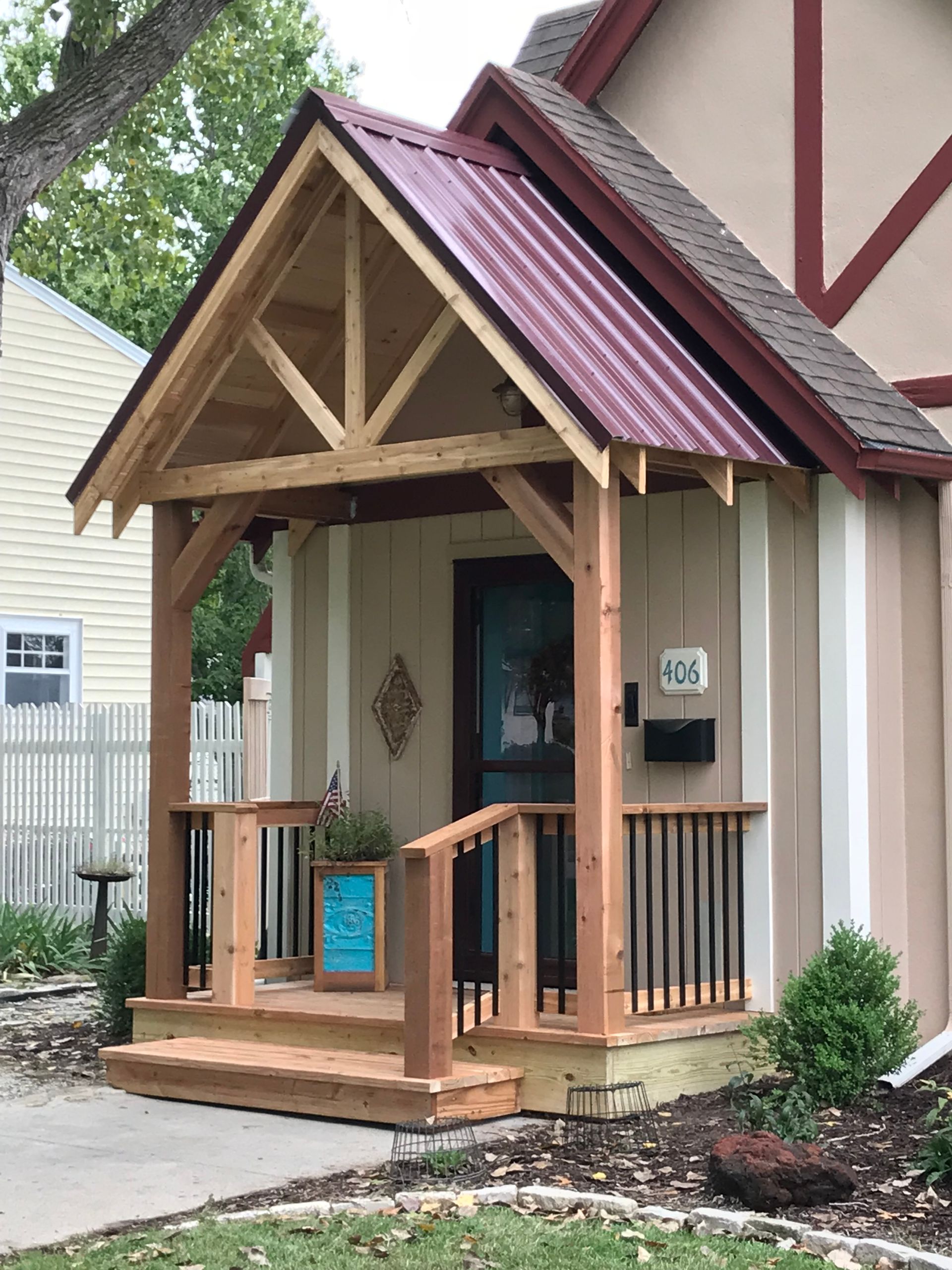 Wooden porch with a red metal roof on a tan house with a black door.