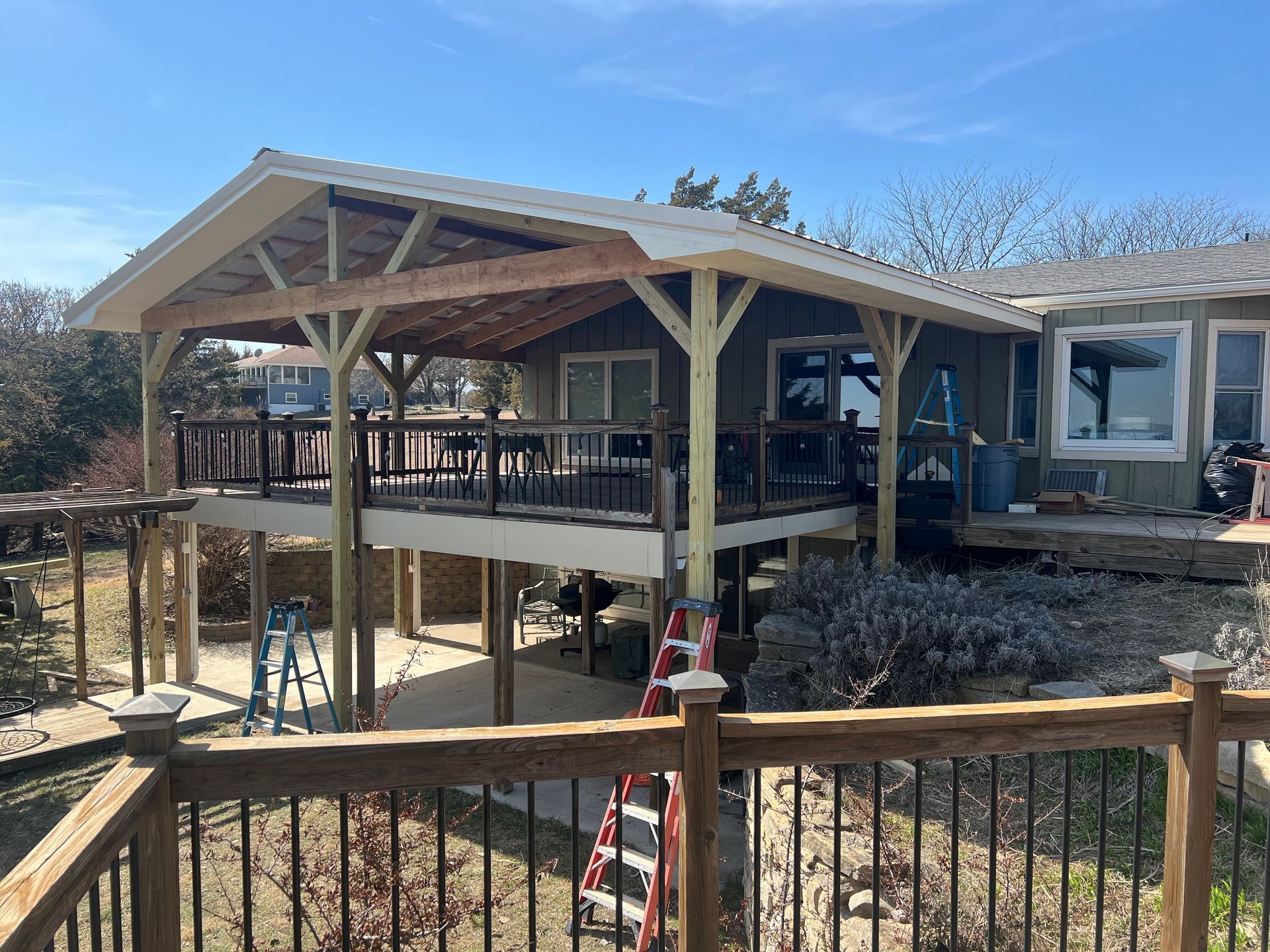 Deck with a covered patio extension; wooden structure with black railing, clear blue sky.