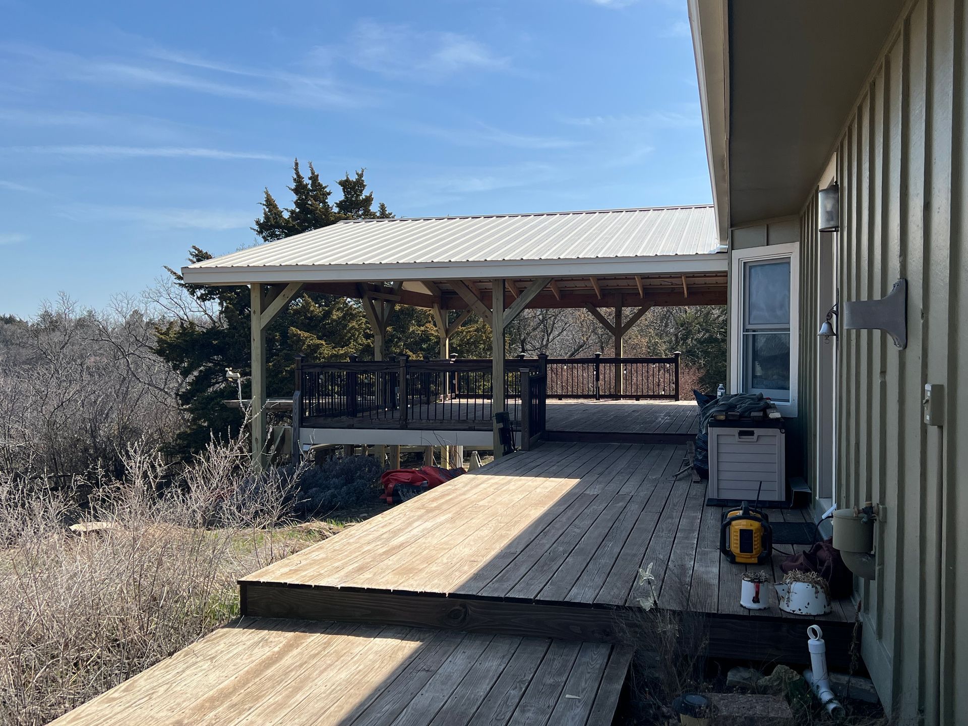 Wooden deck with covered patio attached to a light-colored house. Sunny, outdoor setting.
