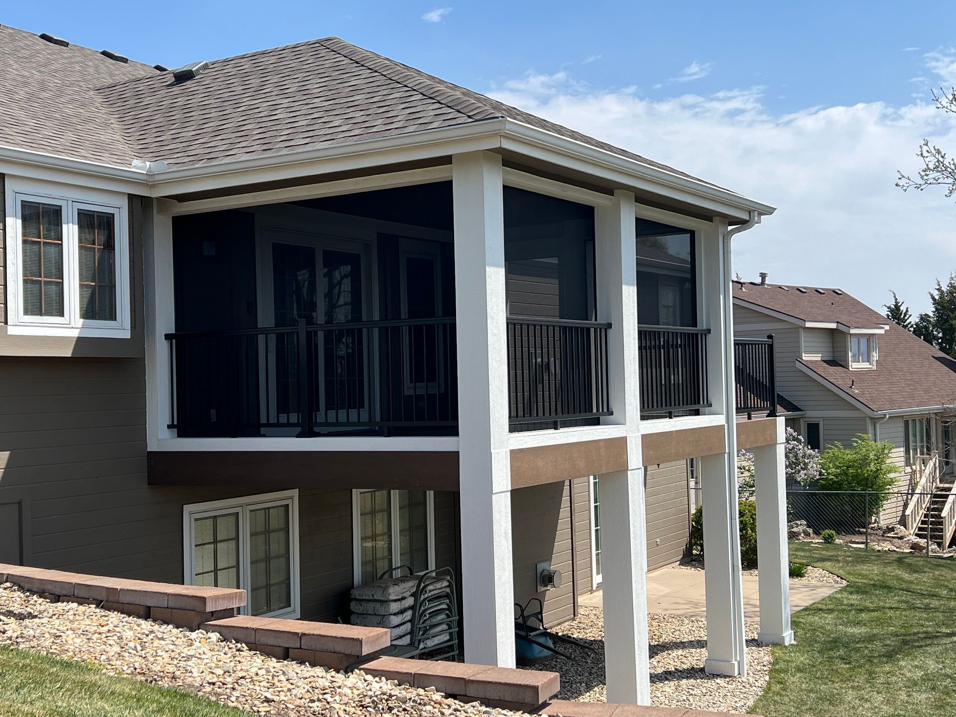 Screened-in porch on a house with white pillars, black screens, and brown roof.