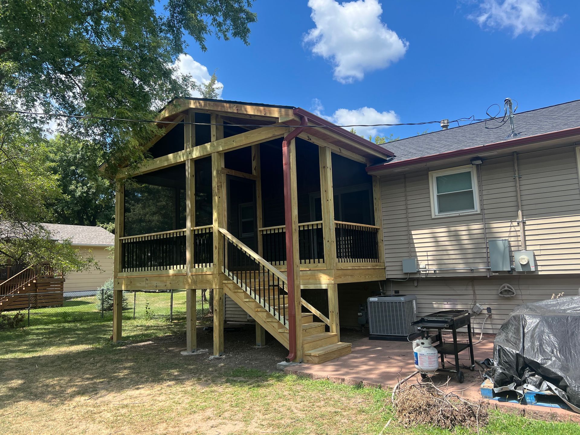 Wooden screened-in porch addition with stairs, attached to a house with a blue sky background.