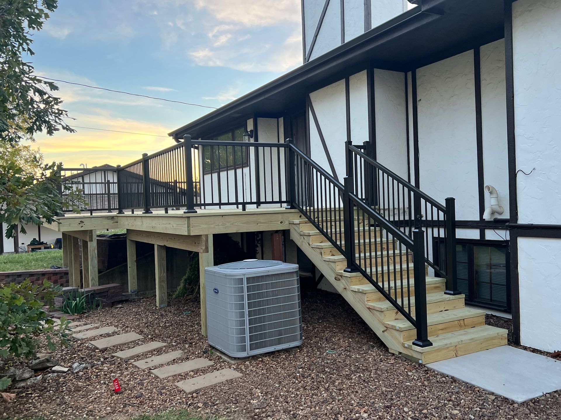 Wooden deck with black railings and stairs. Air conditioning unit sits below deck.