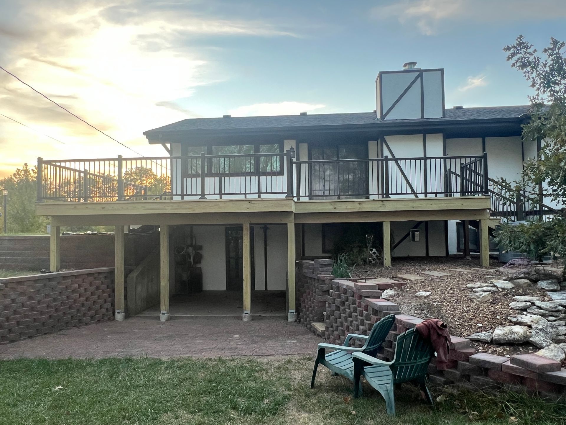 Backyard with a two-story Tudor-style house, featuring a large deck and brick retaining walls.