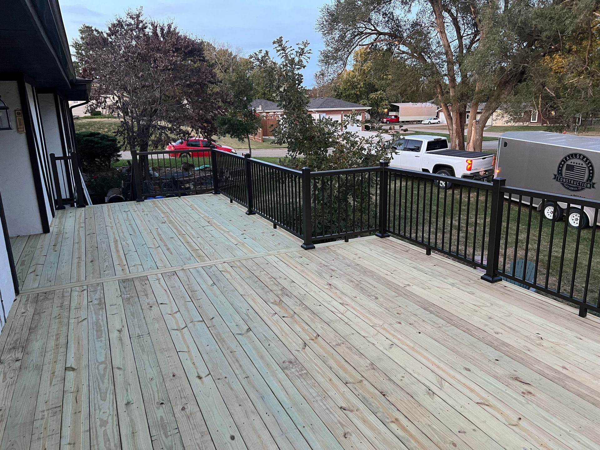 Newly constructed wooden deck with black railings overlooking a suburban neighborhood.