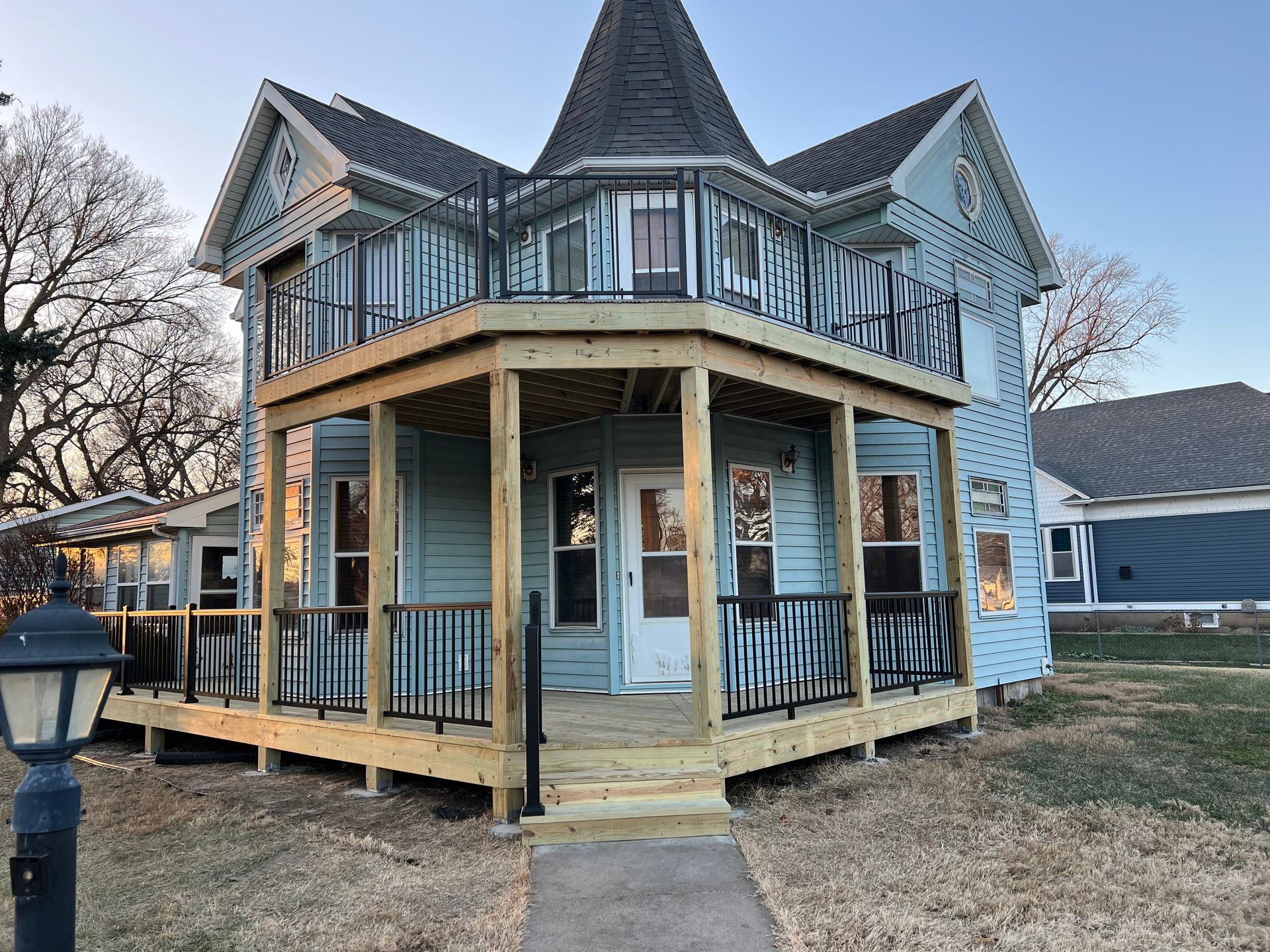 Light blue Victorian house with new wooden porch and black railings.