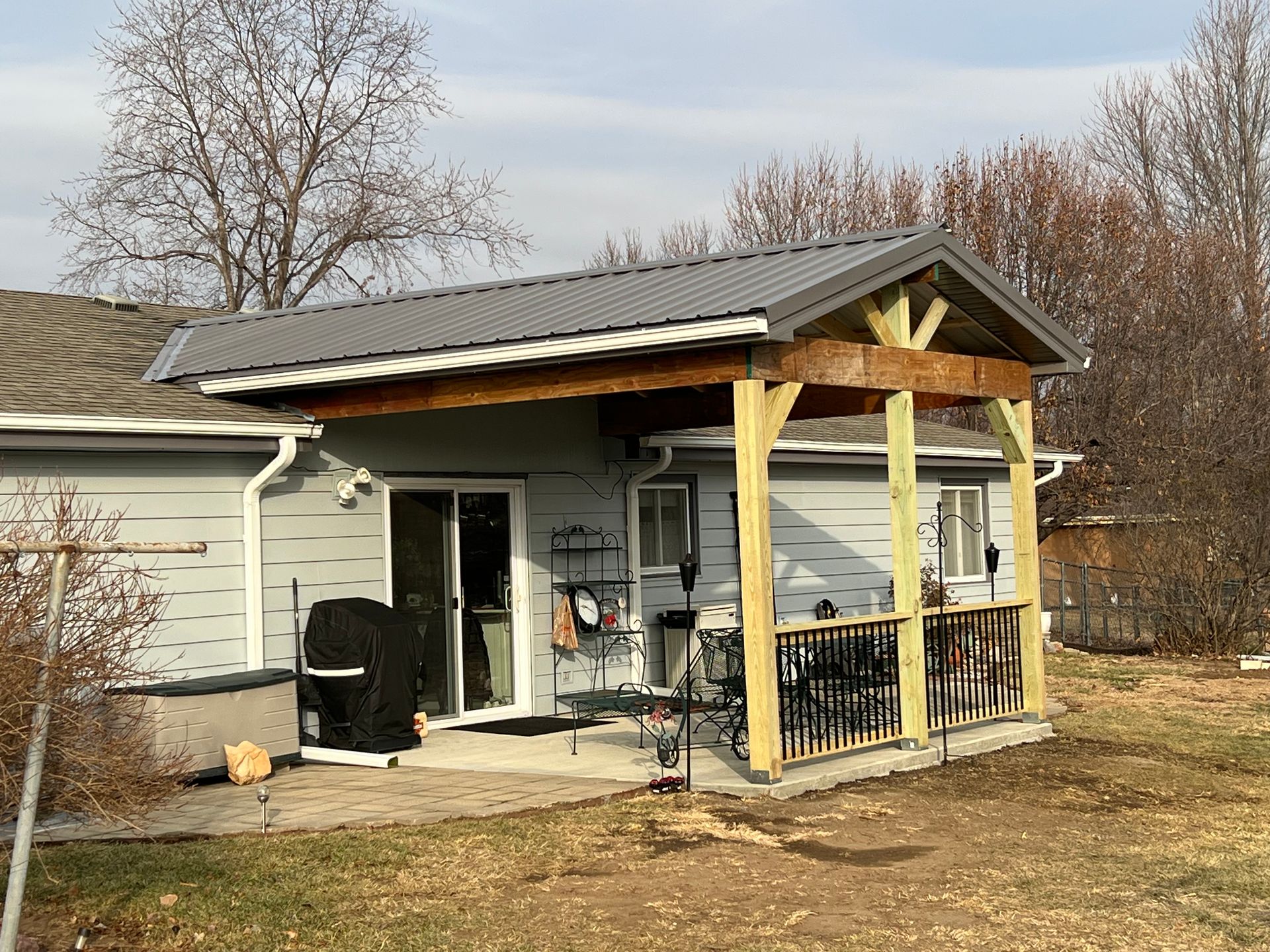 Gray house with wooden porch, metal roof, sliding door, and outdoor grill.