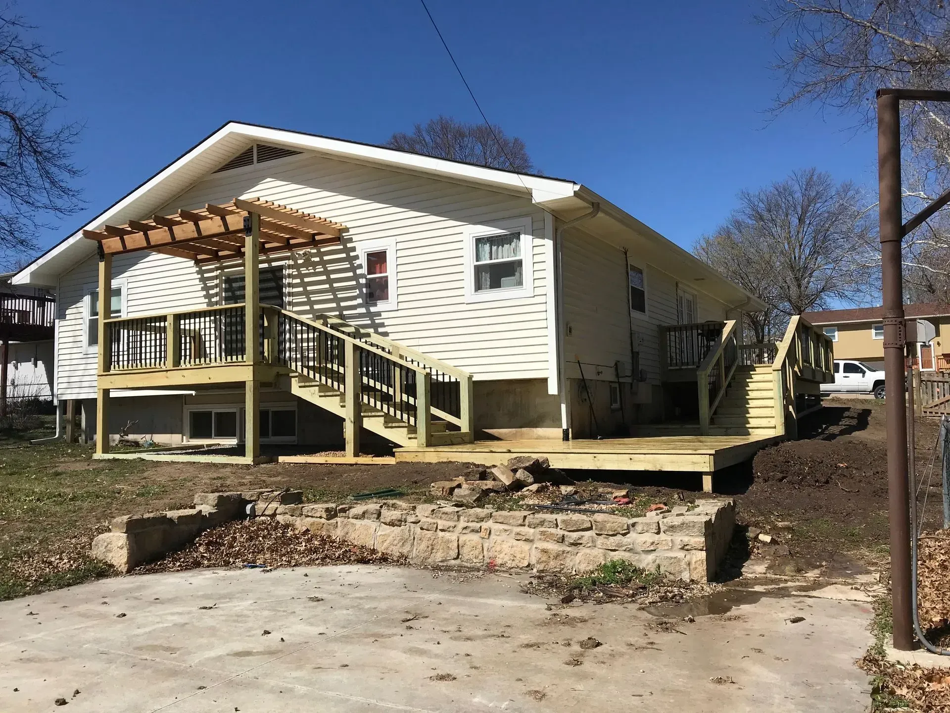 Back view of a white house with a new wooden deck and stairs. Arbor on the deck, sunny day.