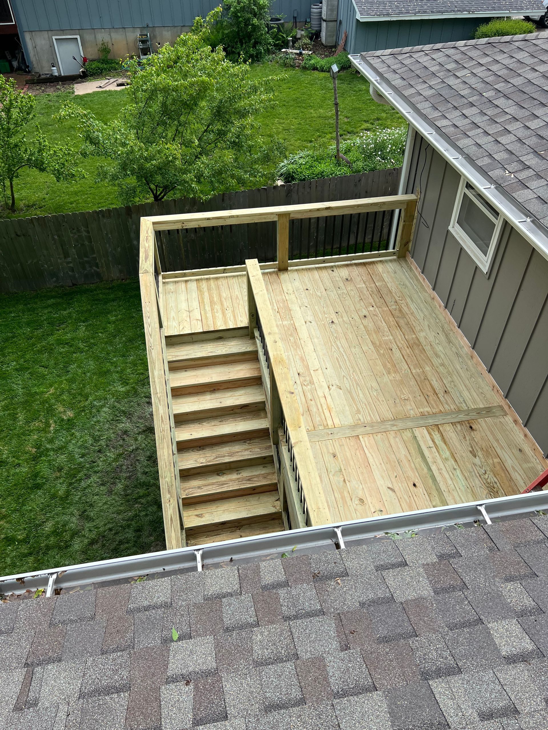 Wooden deck with stairs, attached to a light-colored house, next to green grass.