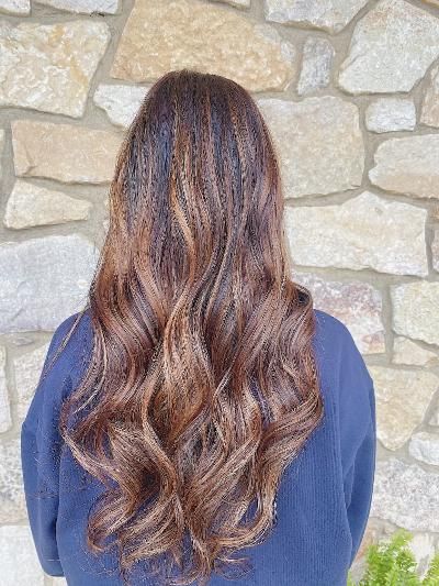 A woman with long brown hair is standing in front of a stone wall