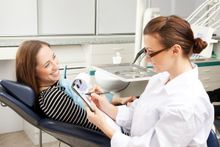 A woman is sitting in a dental chair talking to a dentist.