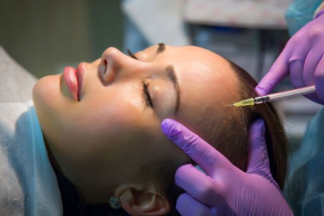 A woman is getting a botox injection in her forehead