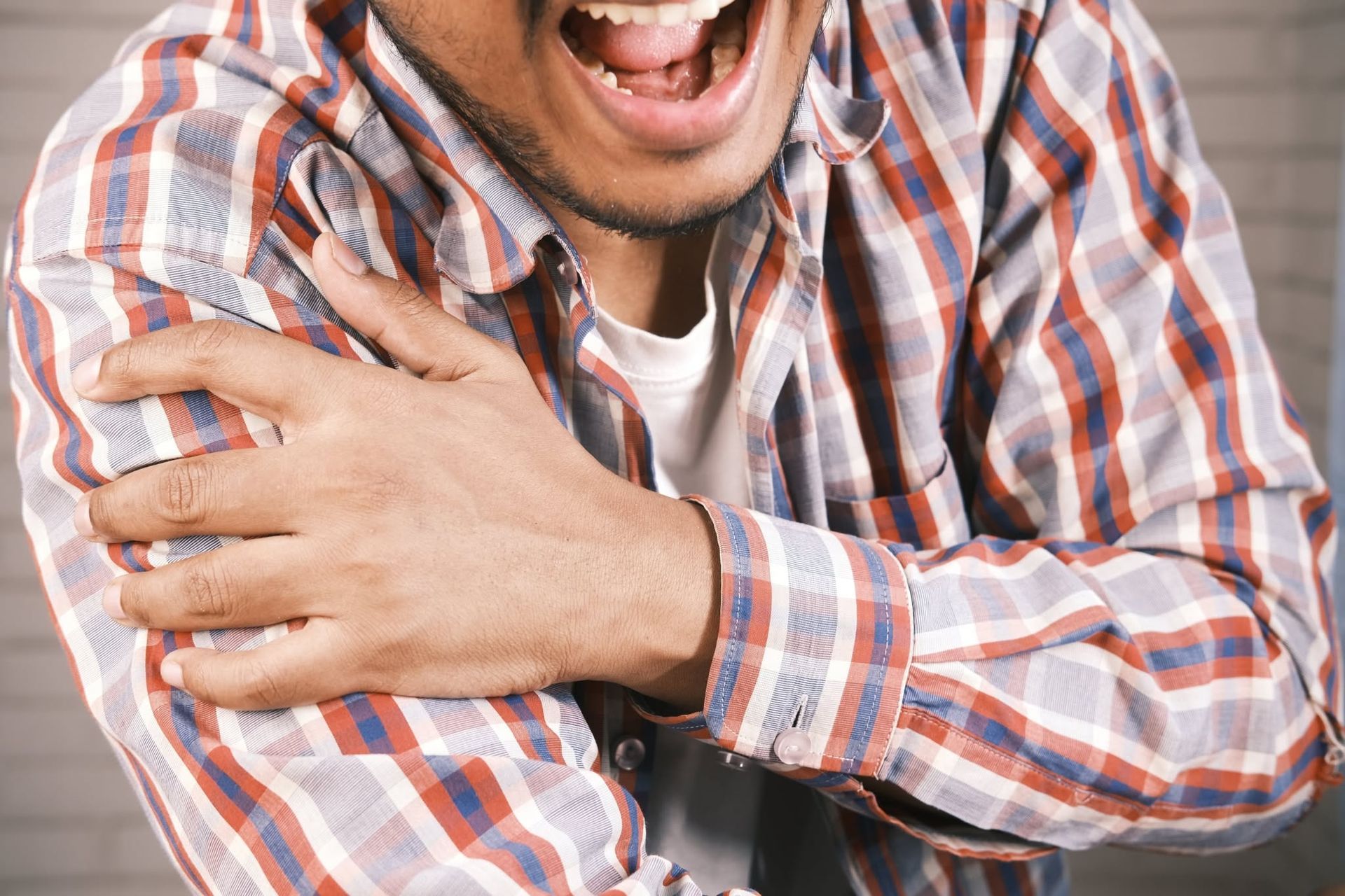 Close-up of a person in a plaid shirt clutching their shoulder and laughing.