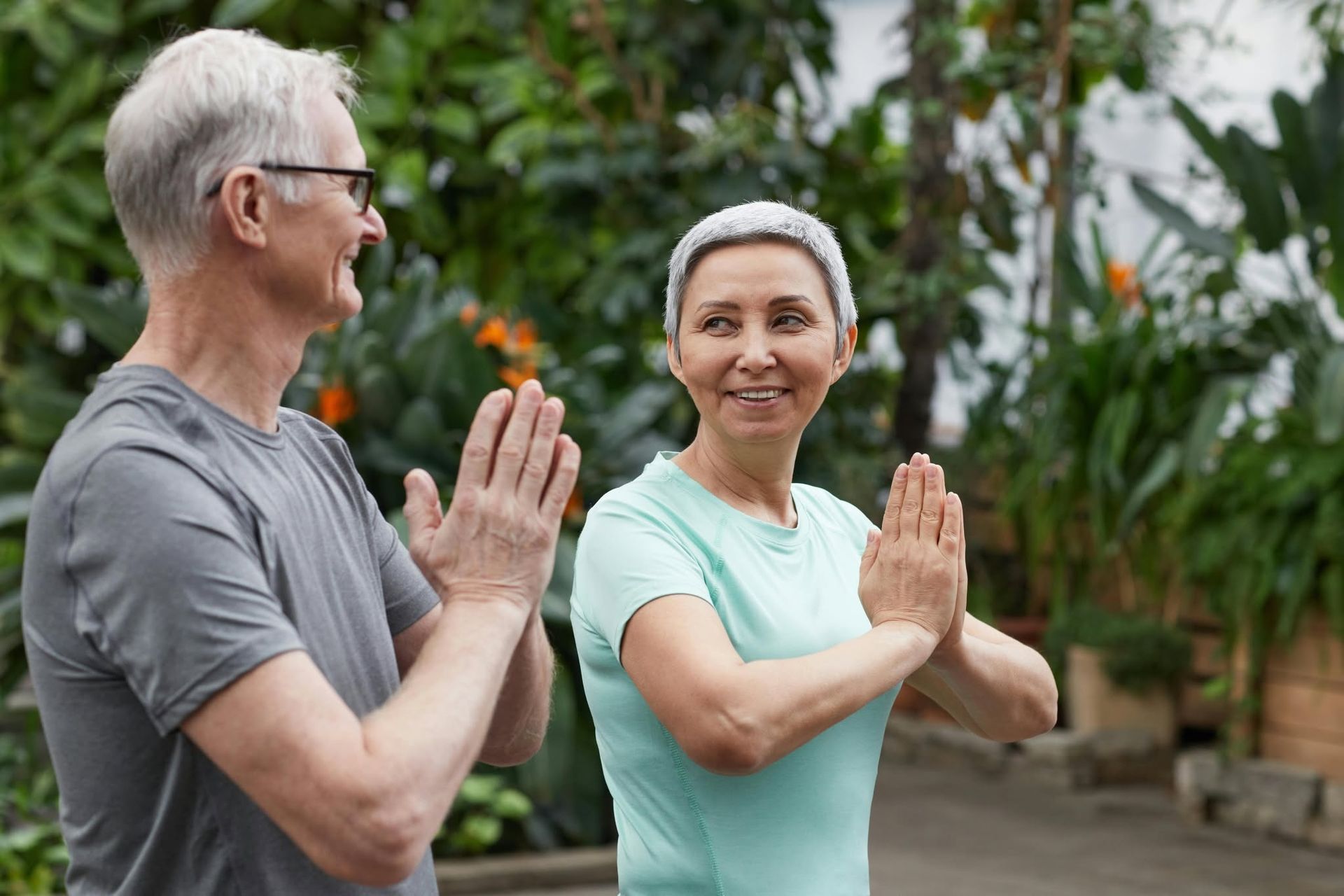 Two people practicing a standing hand pose outdoors in a garden.
