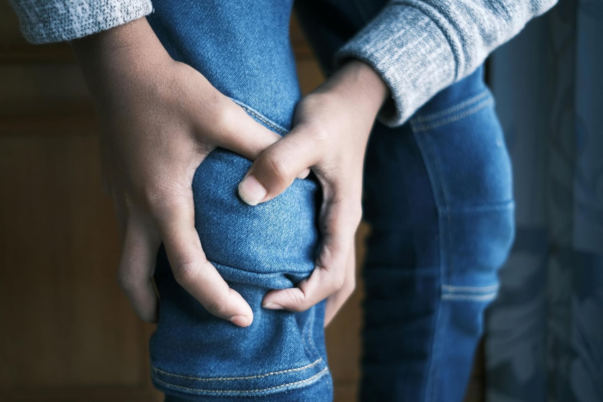 Hands clasping a blue-jeans-covered knee in a close-up indoor shot