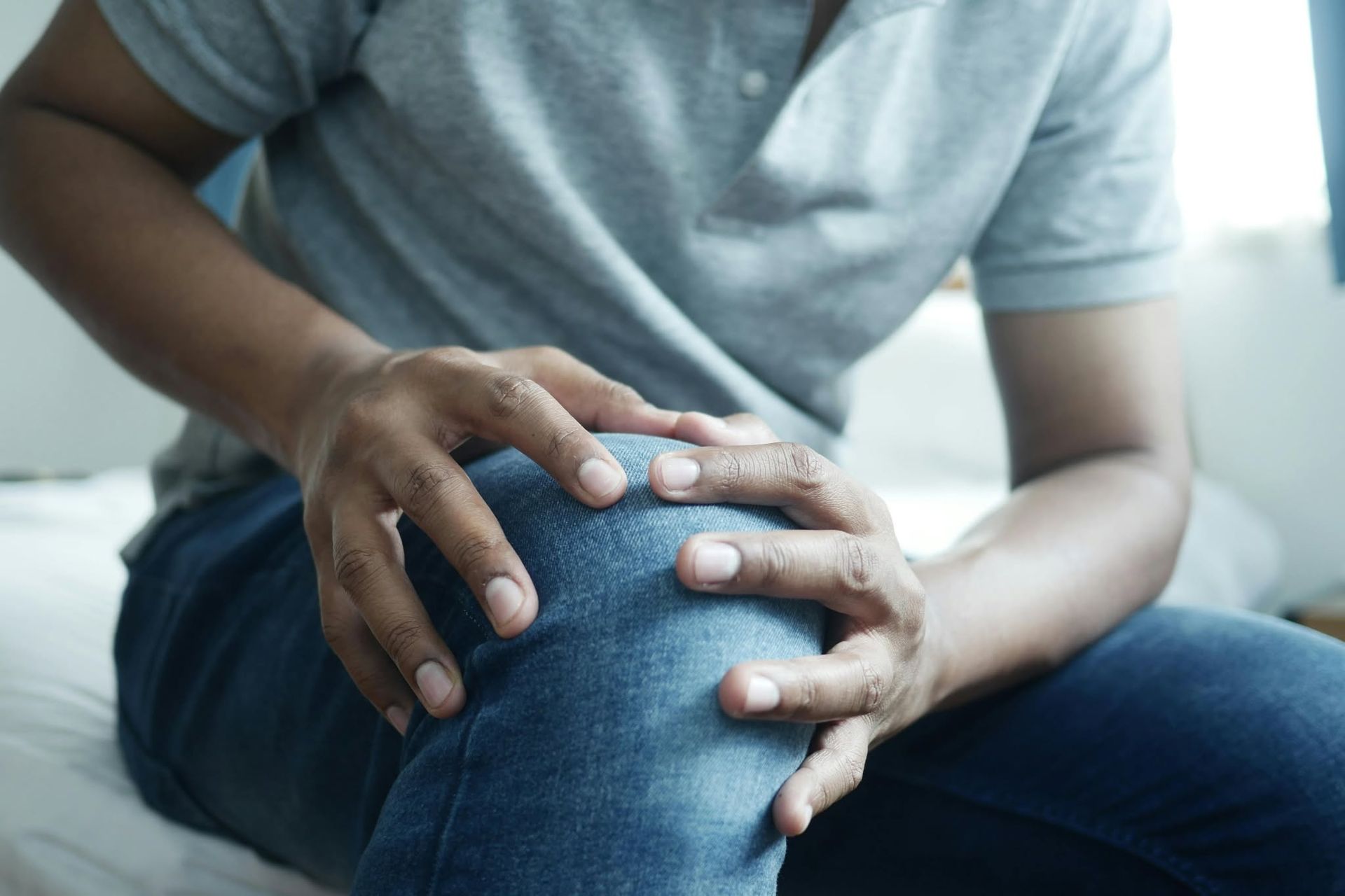 Person holding a knee with both hands, suggesting knee pain or injury.