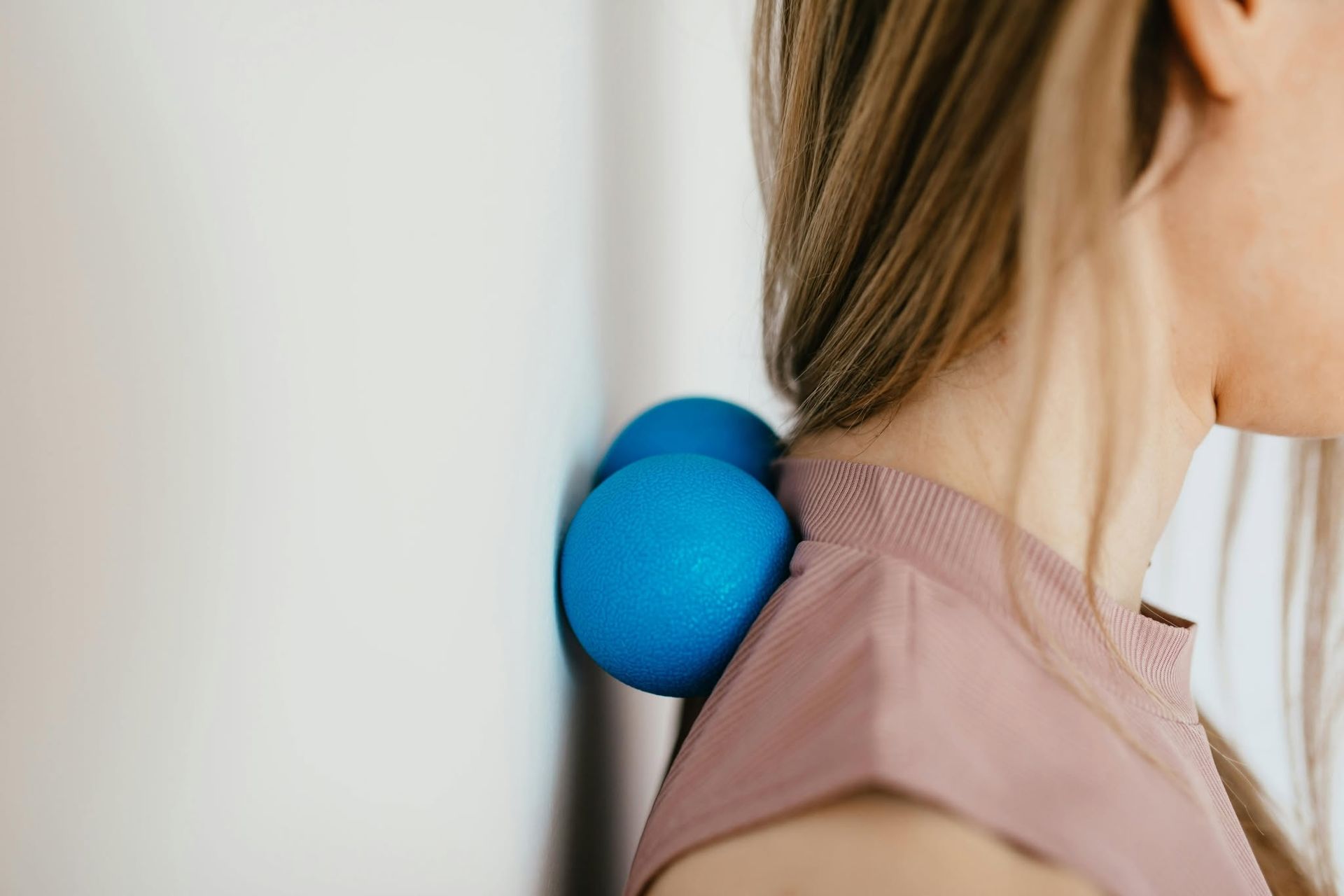 Blue massage balls pressing into the back of a person’s neck near a white wall