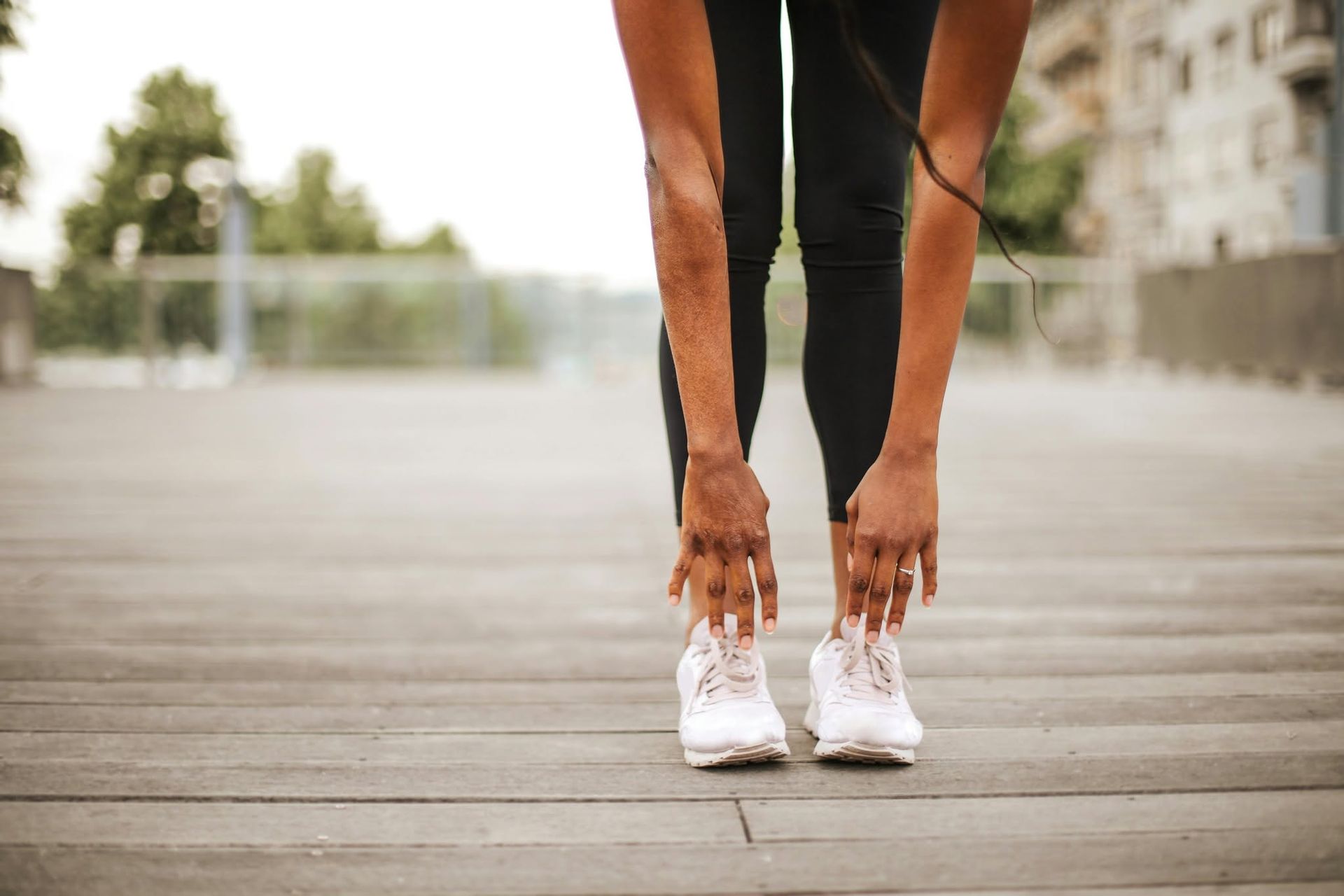 Runner bending to touch white shoes on a wooden boardwalk outdoors