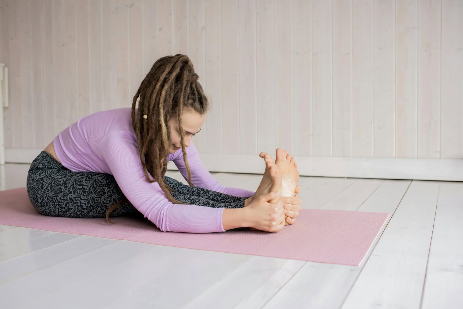 Person doing seated forward bend on a pink mat in a bright room