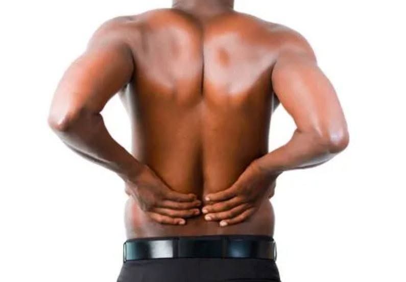 Bare-backed person holding their lower back with both hands, suggesting back pain.