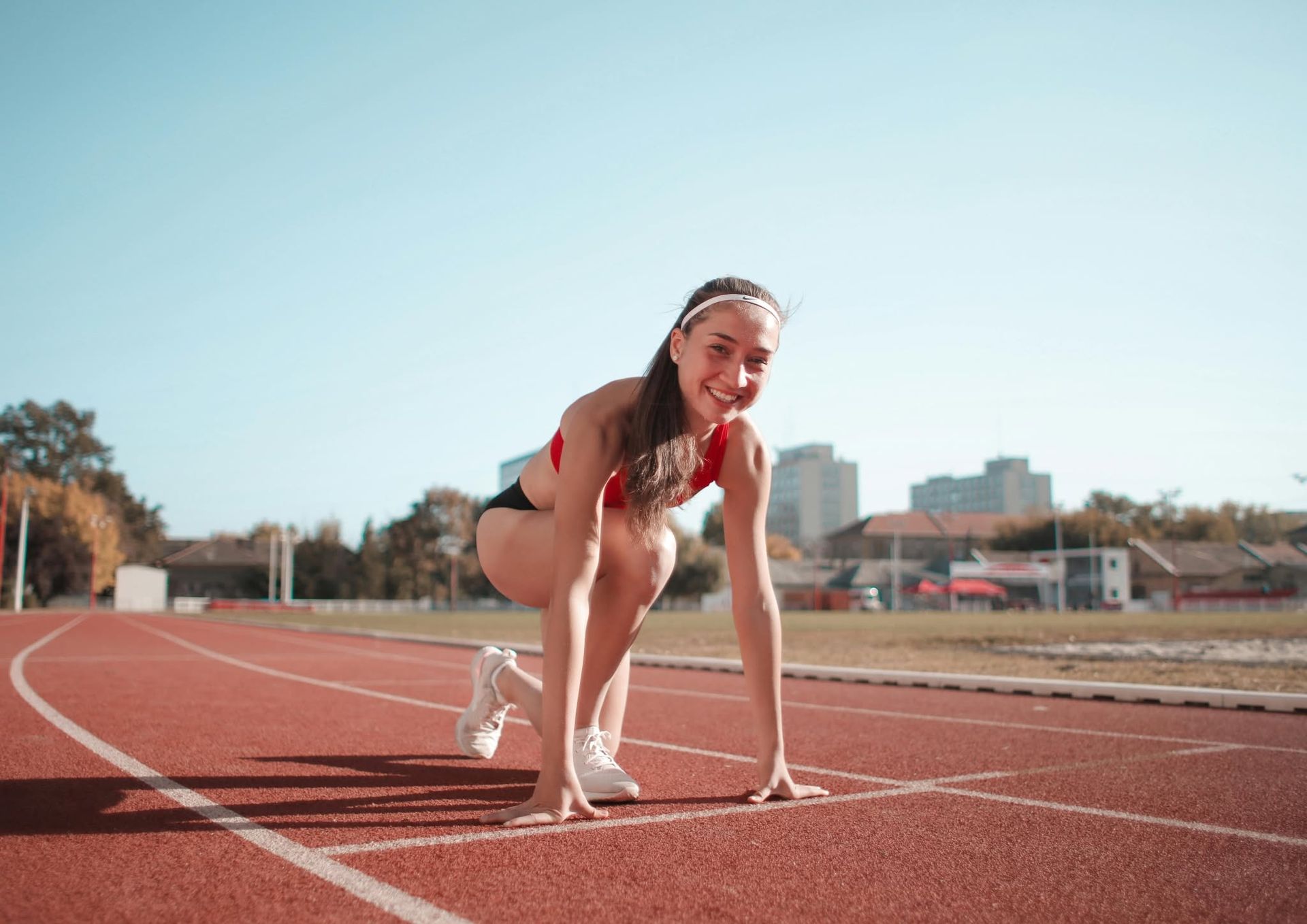 Runner crouched at a starting line on a red track under a clear blue sky
