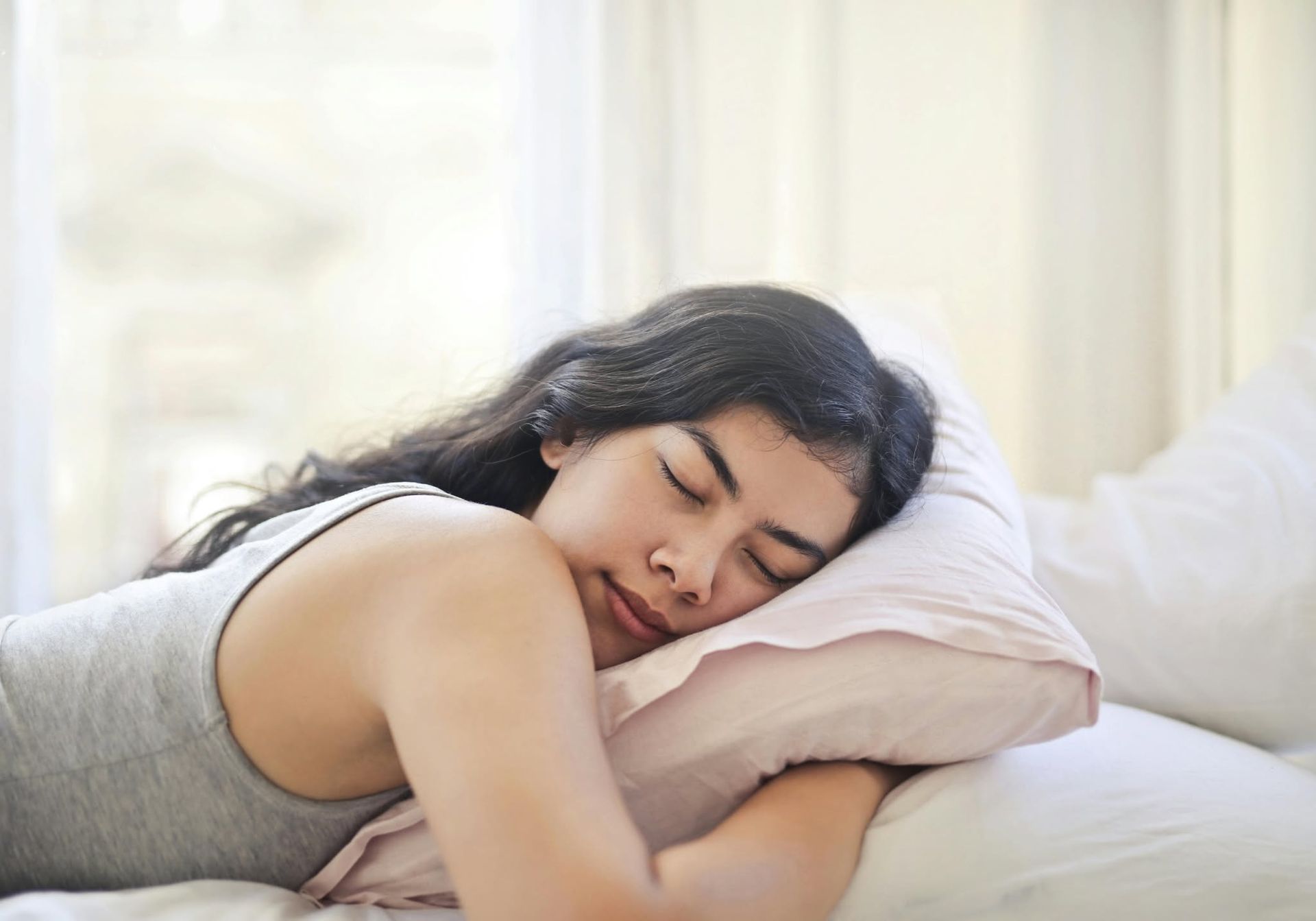 Person sleeping on a bed with a white pillow in soft morning light.