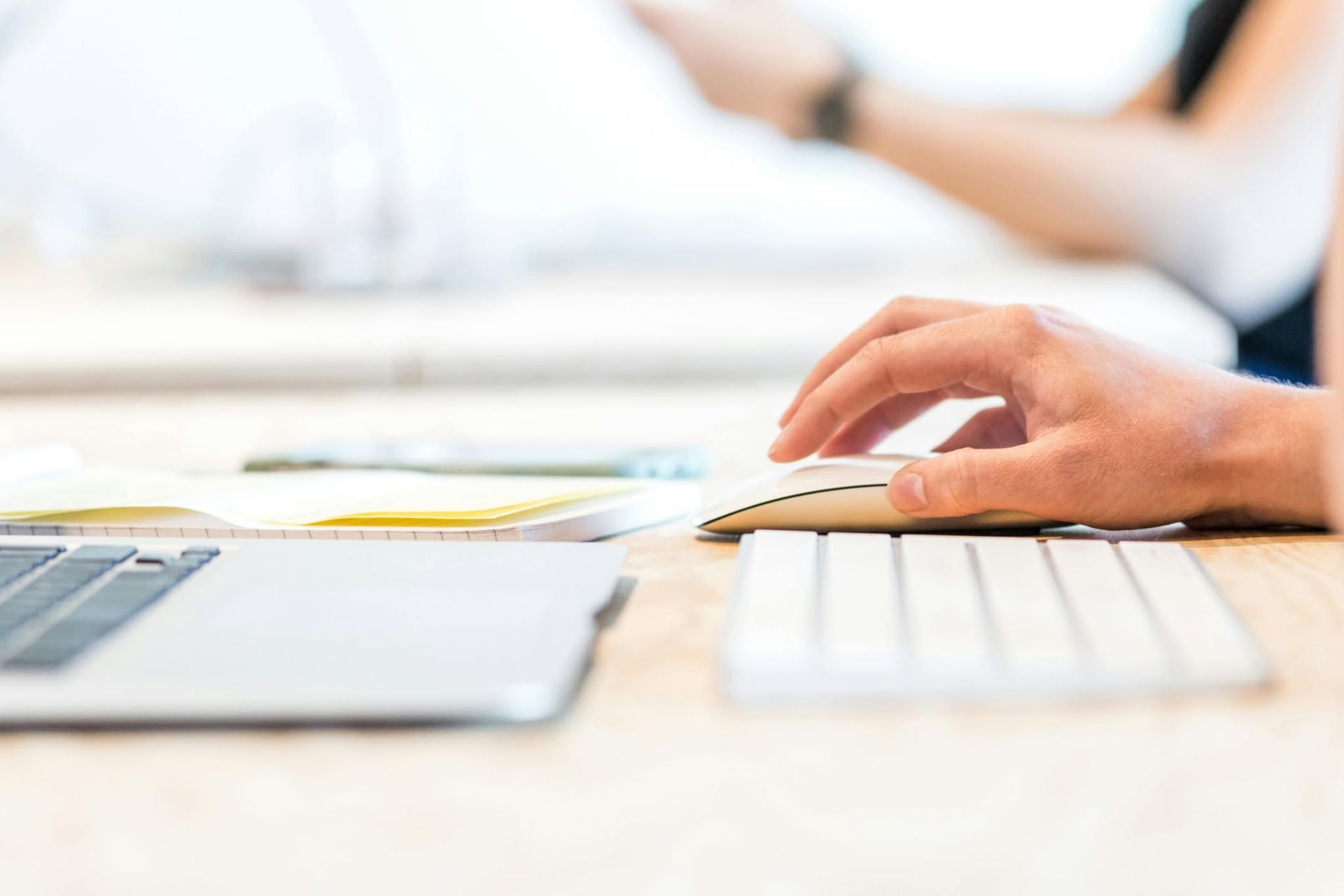 Hands typing on a keyboard beside a laptop in a bright office workspace