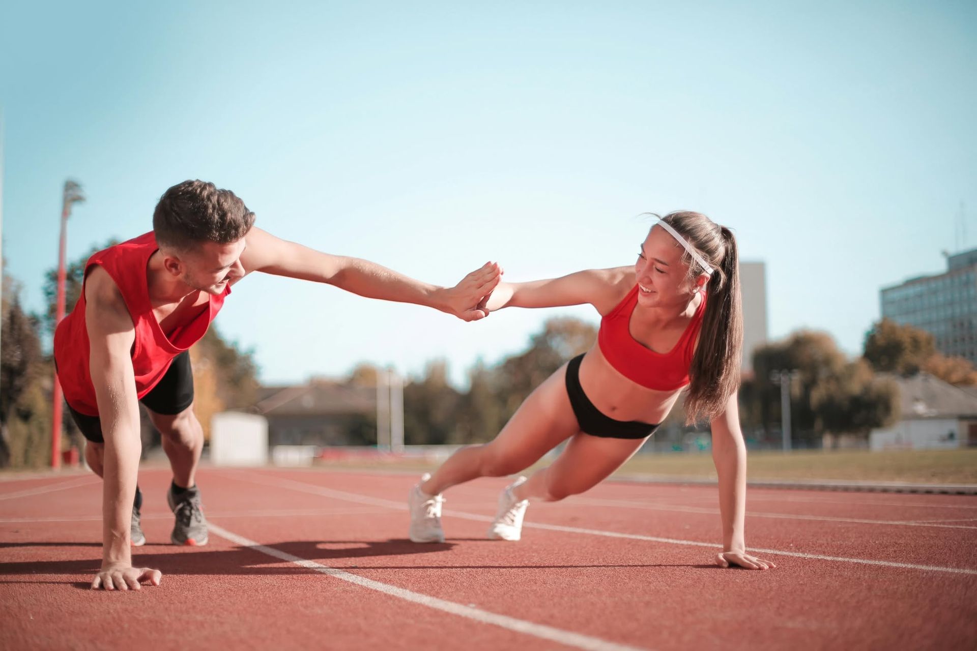 Two runners in red sportswear high-five while stretching on a track outdoors