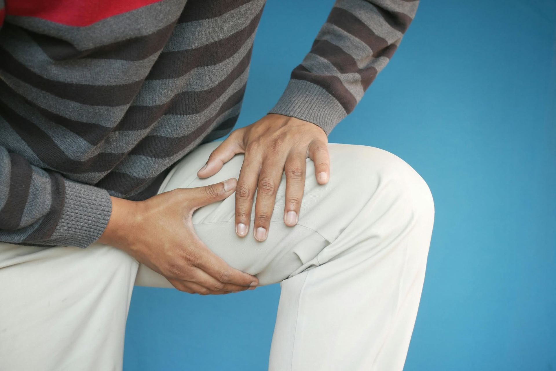 Person holding a painful knee while seated against a blue background