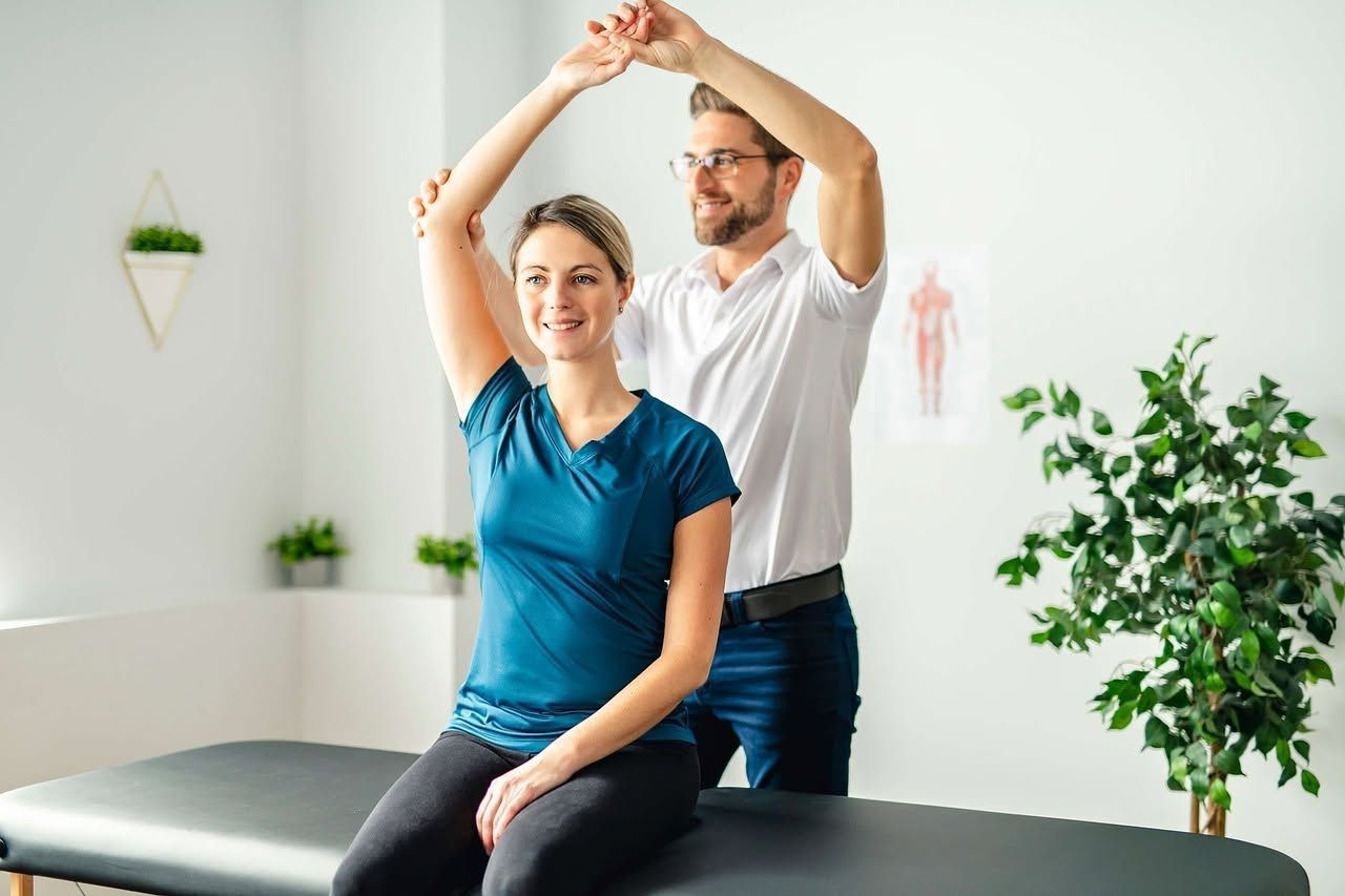 Physical therapist guiding a seated patient through a shoulder stretch in a bright clinic room