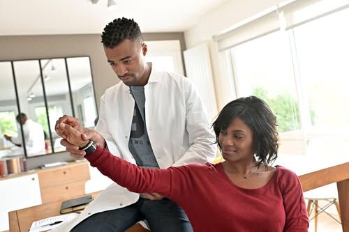 Doctor examining a seated patient’s wrist in a bright clinic room