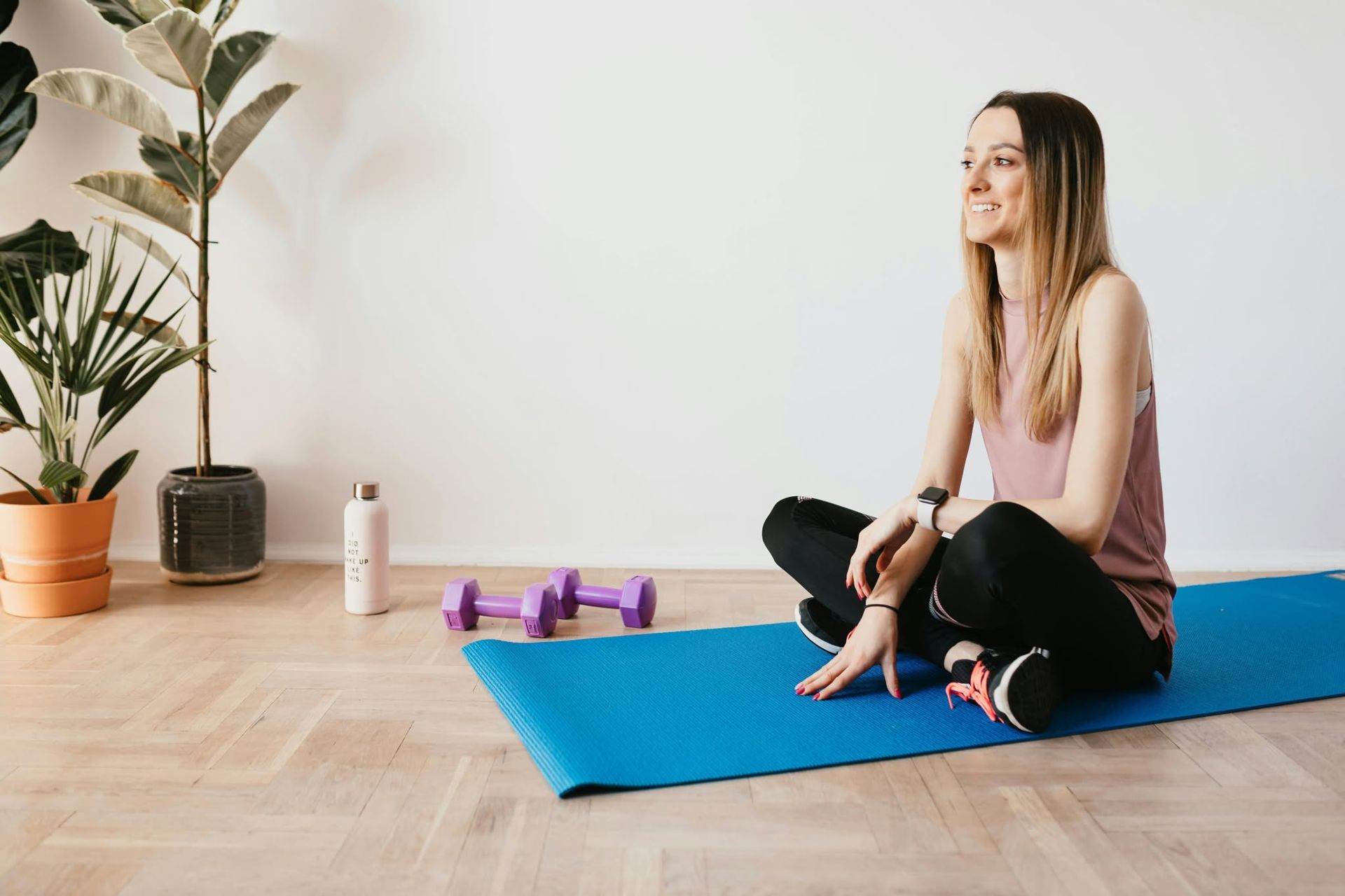 Woman sitting on a blue yoga mat beside purple dumbbells in a bright room