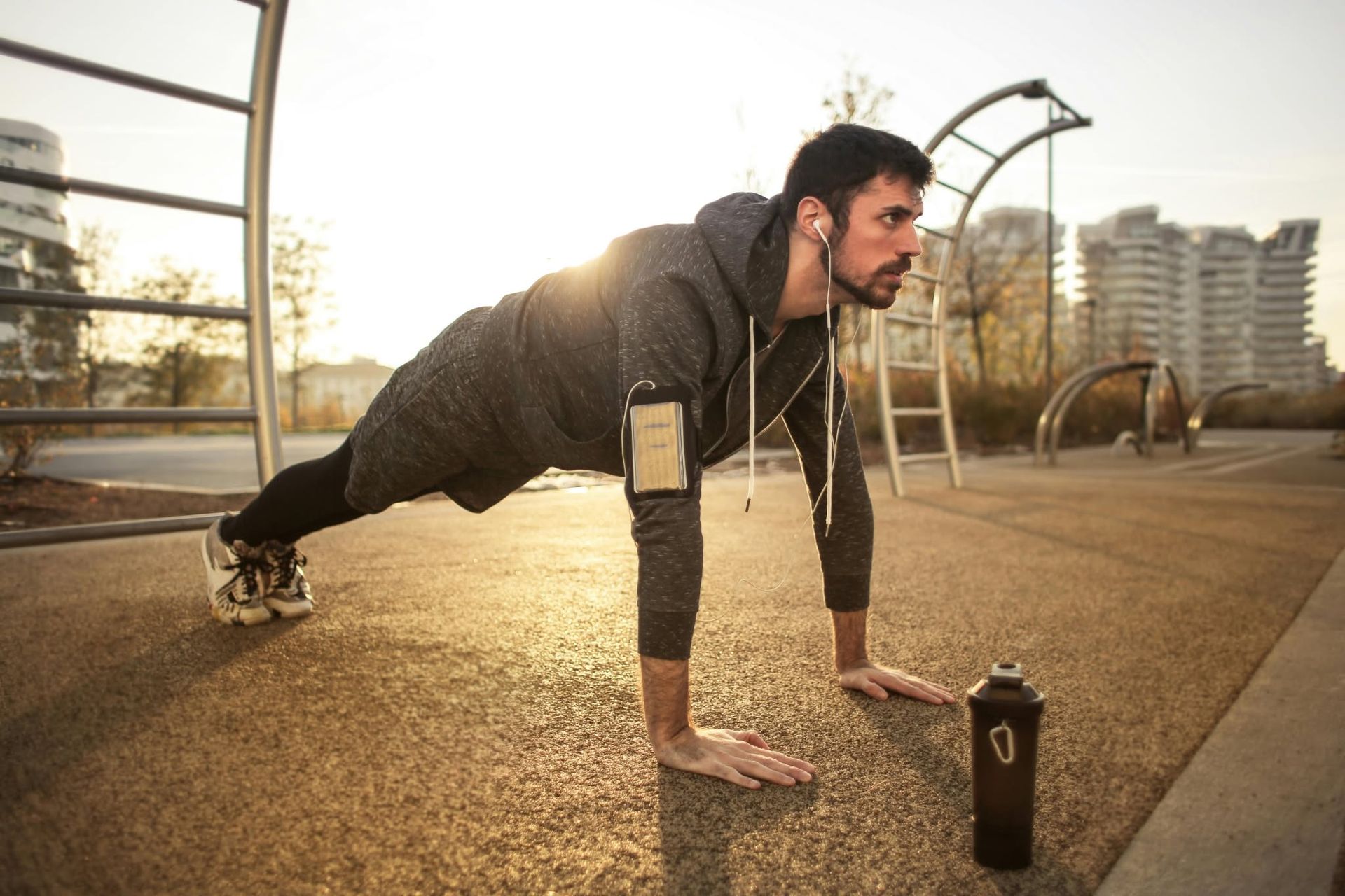 Man doing a plank workout on an outdoor court at sunset, with a water bottle nearby