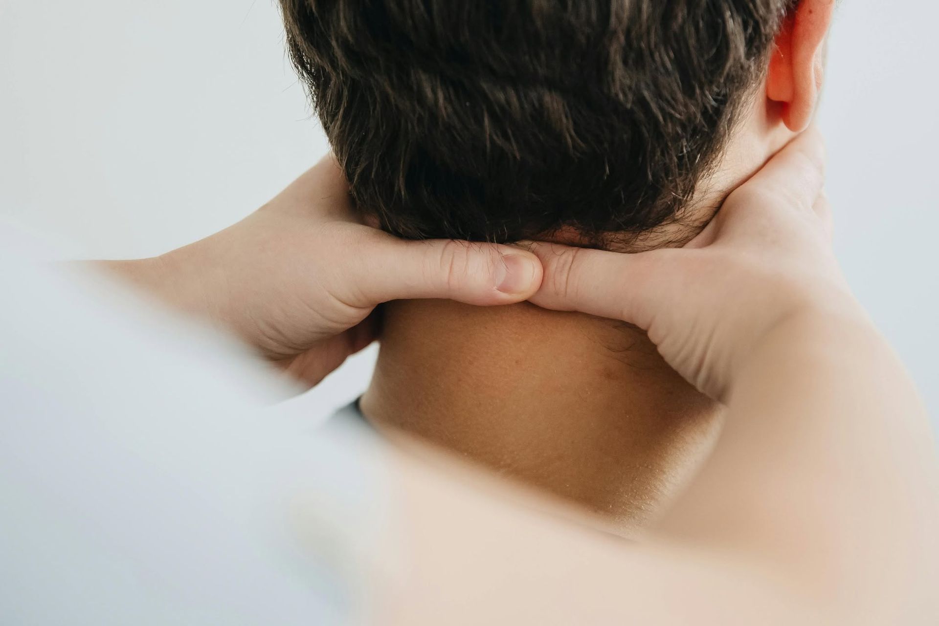 Hands holding the back of a person's neck, suggesting neck massage or pain relief.