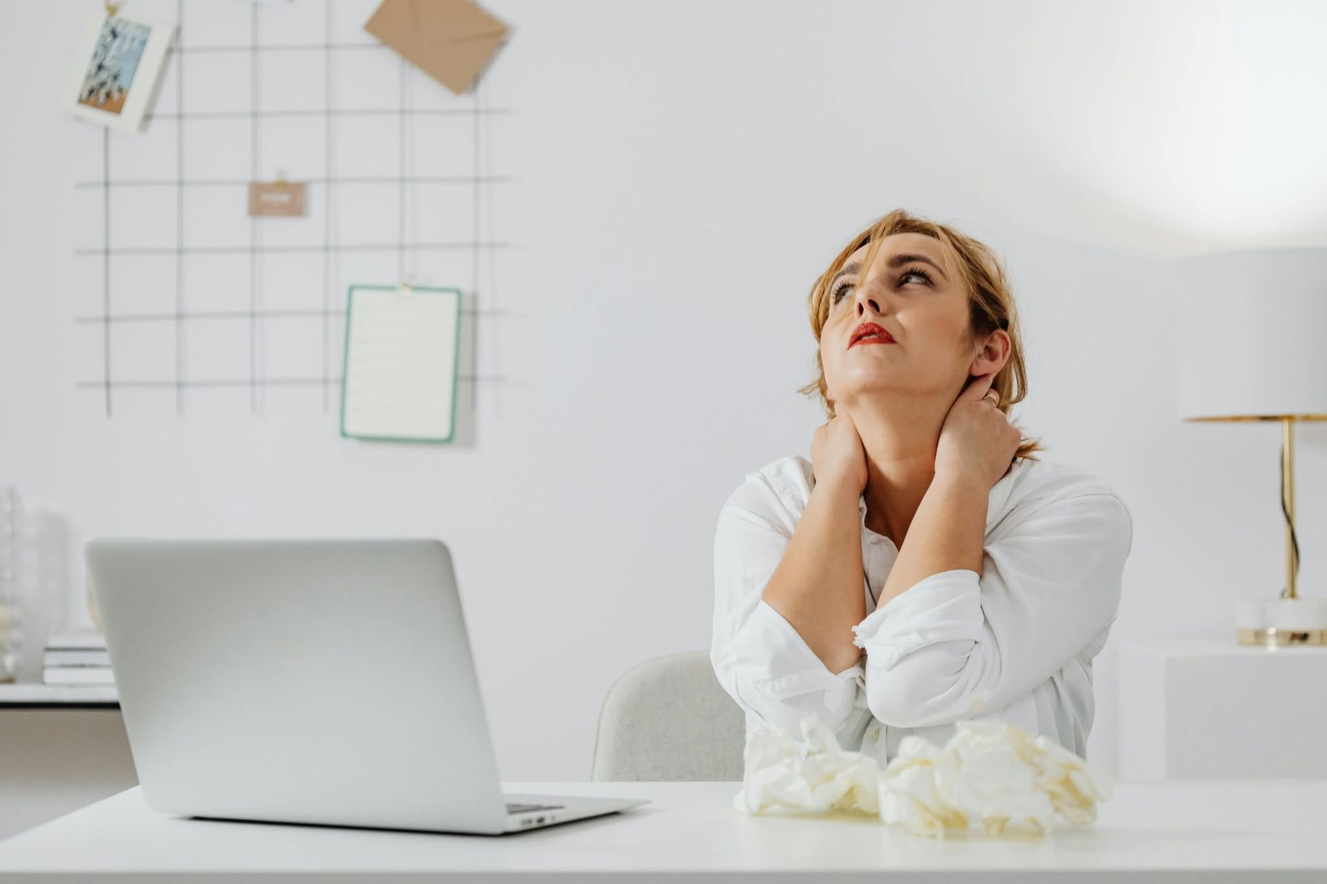 Woman at a desk with a laptop, gazing upward thoughtfully in a bright minimalist office