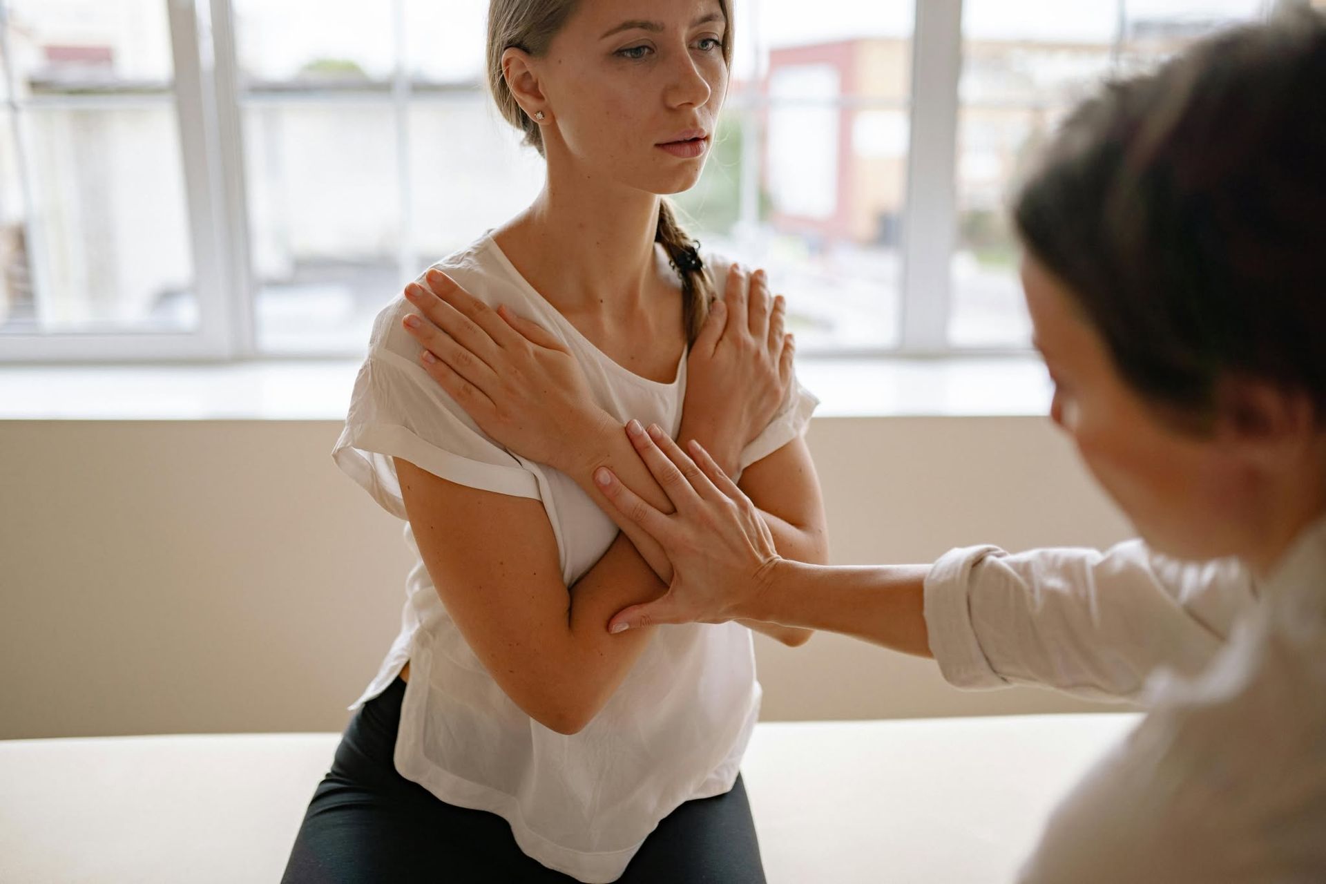 Physical therapist guiding a patient through a shoulder stretch in a bright clinic room