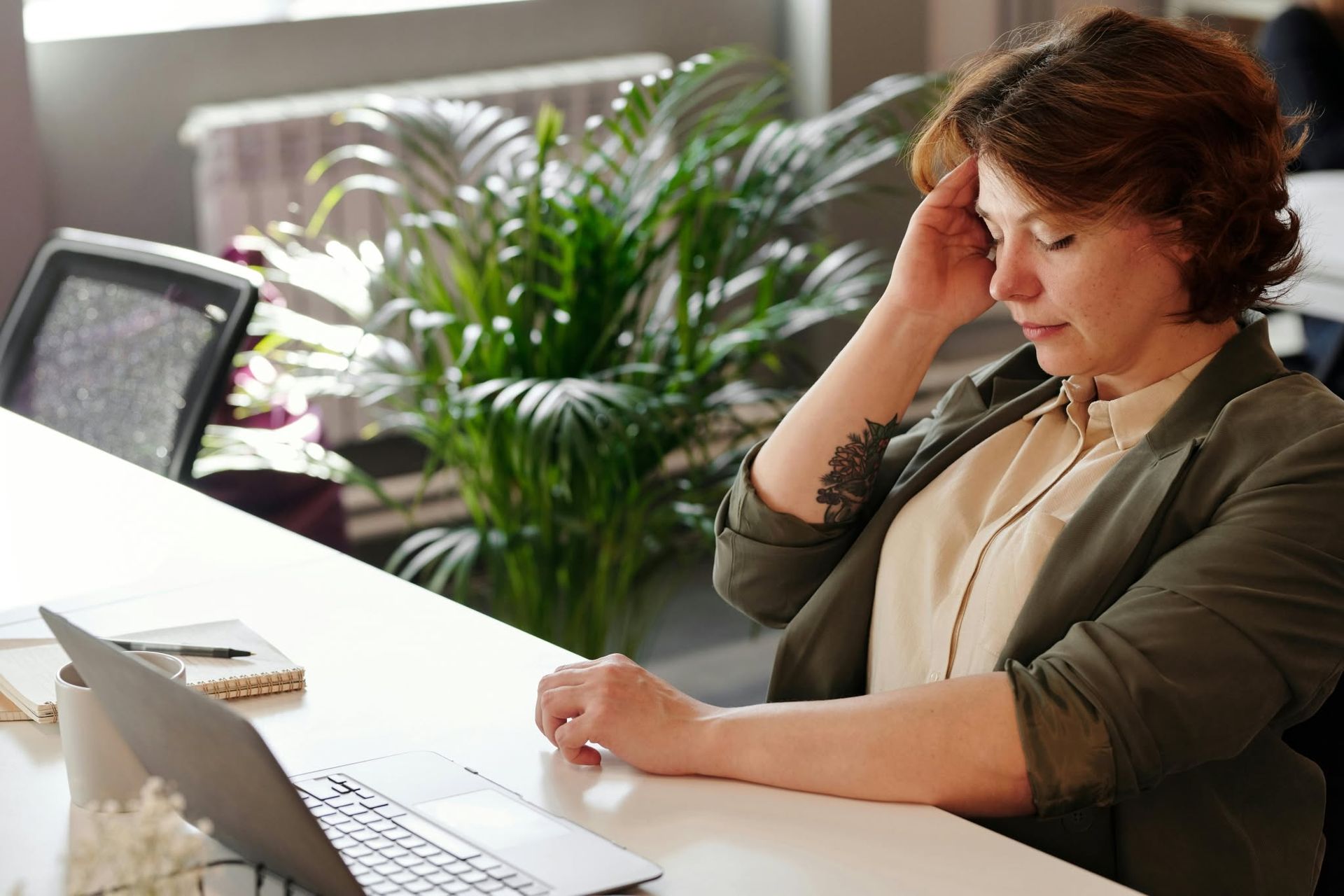 Woman sitting at a desk, talking on the phone beside an open laptop in a bright office