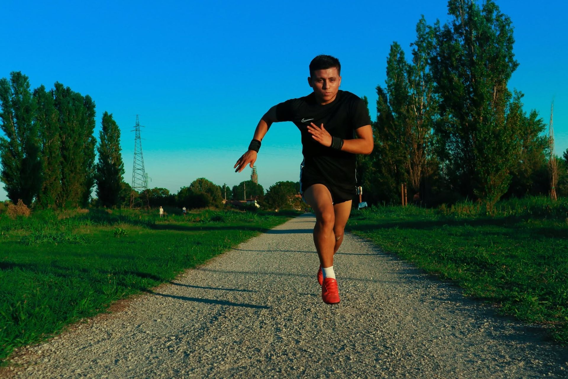 Runner sprinting on a gravel path through a green park under a bright blue sky