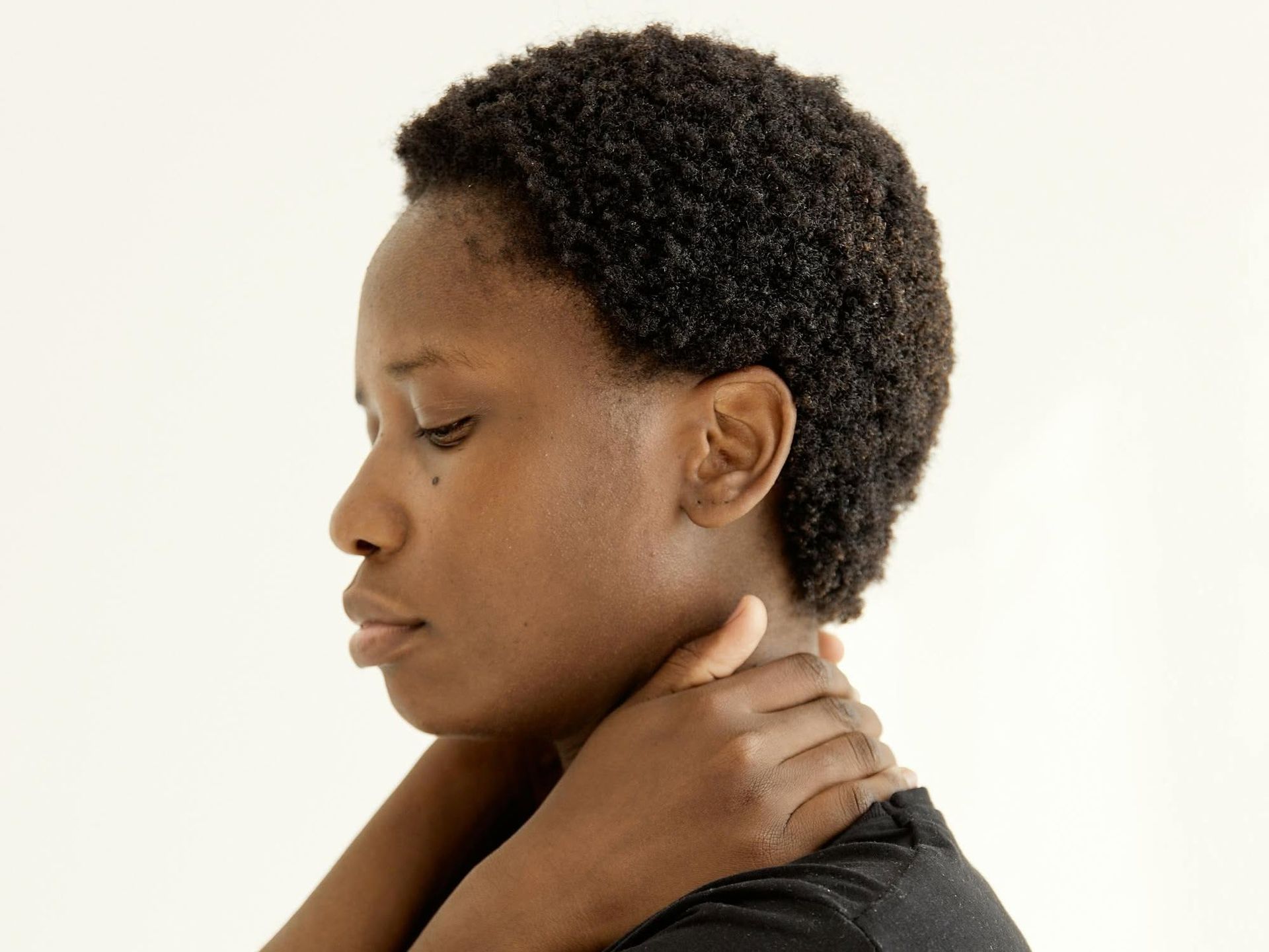 Person holding their neck and shoulder, looking down in profile against a plain background.