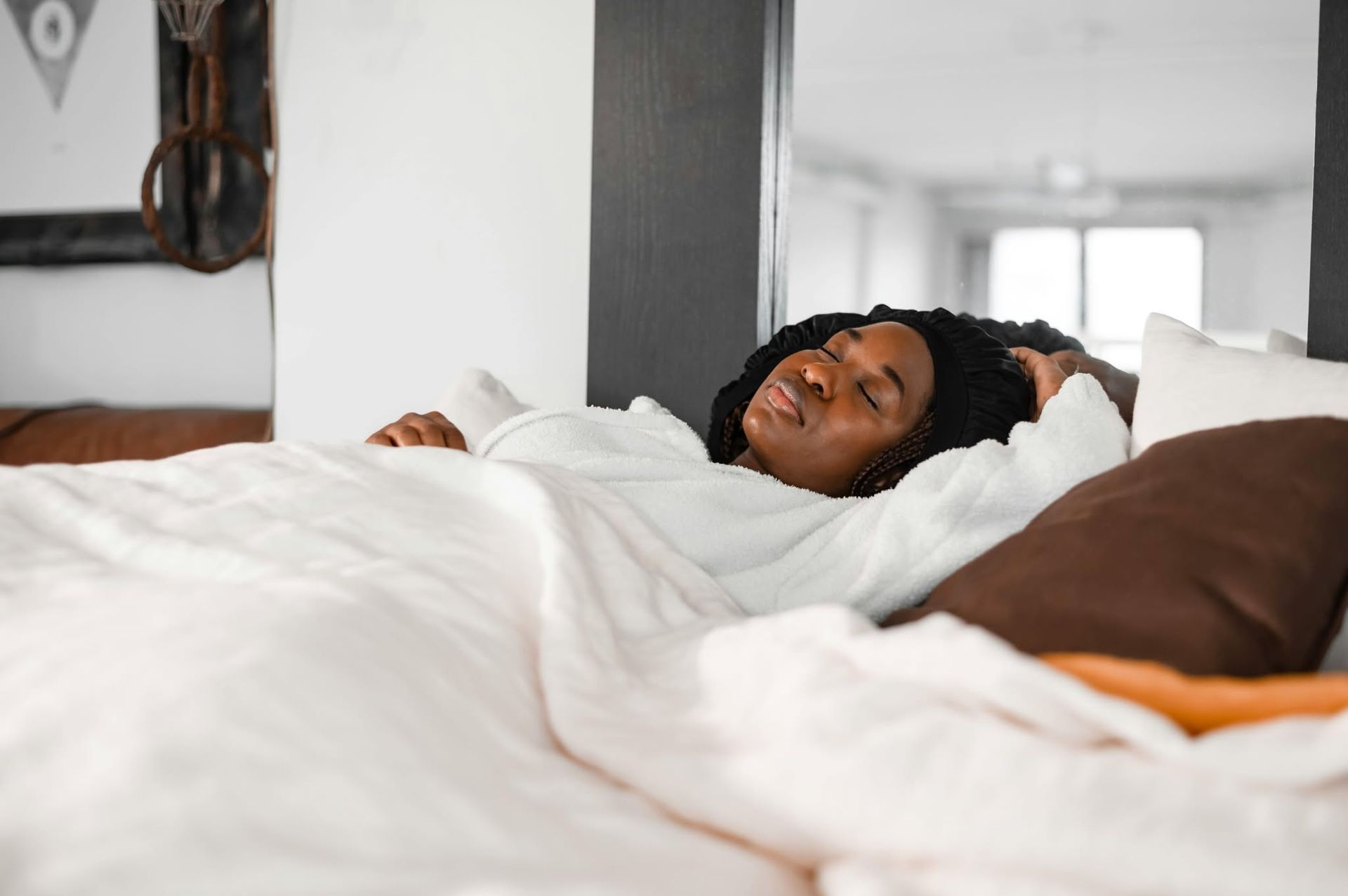 Person resting in a bed with white bedding in a bright, modern bedroom