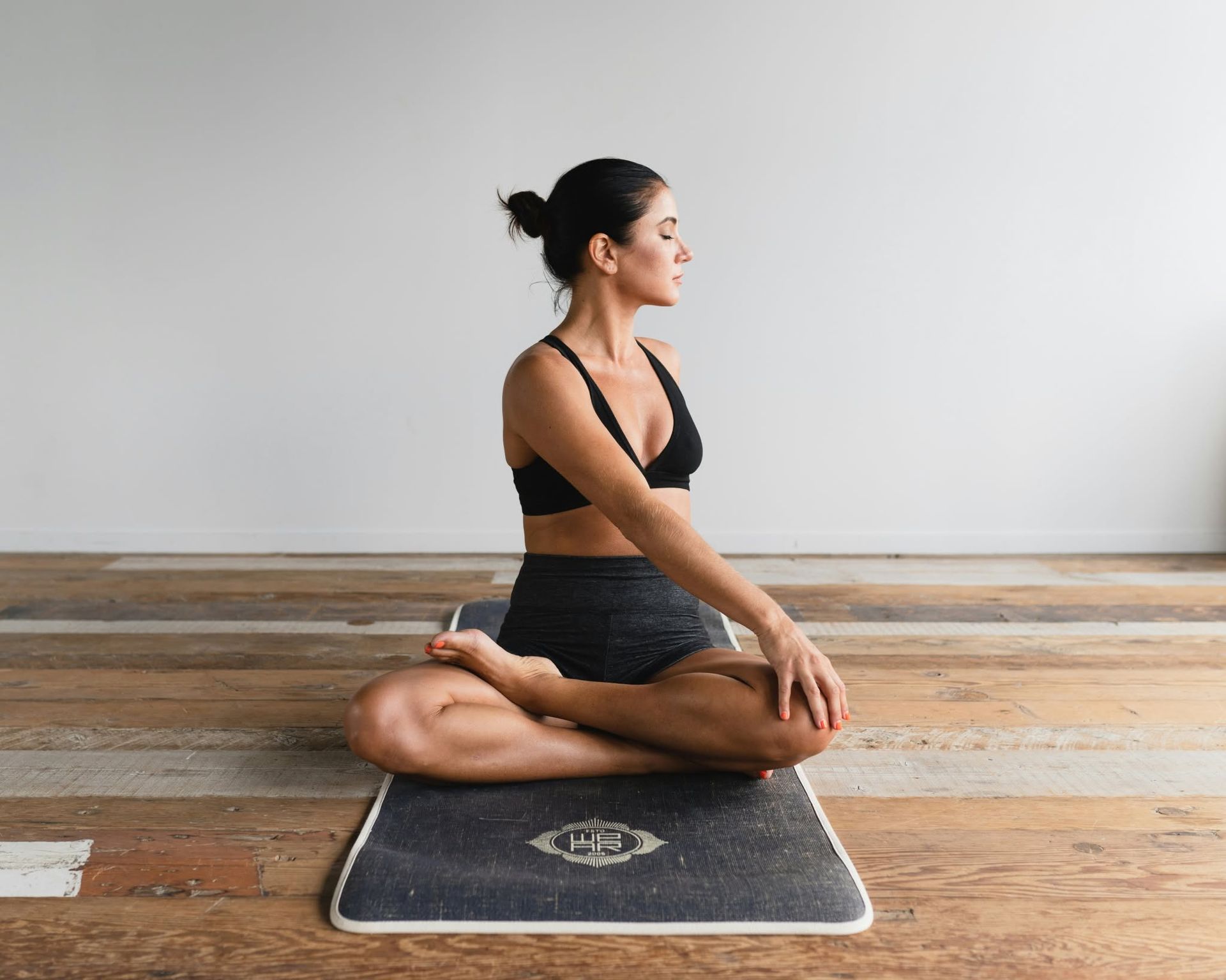Woman seated cross-legged on a yoga mat, facing sideways in a calm studio