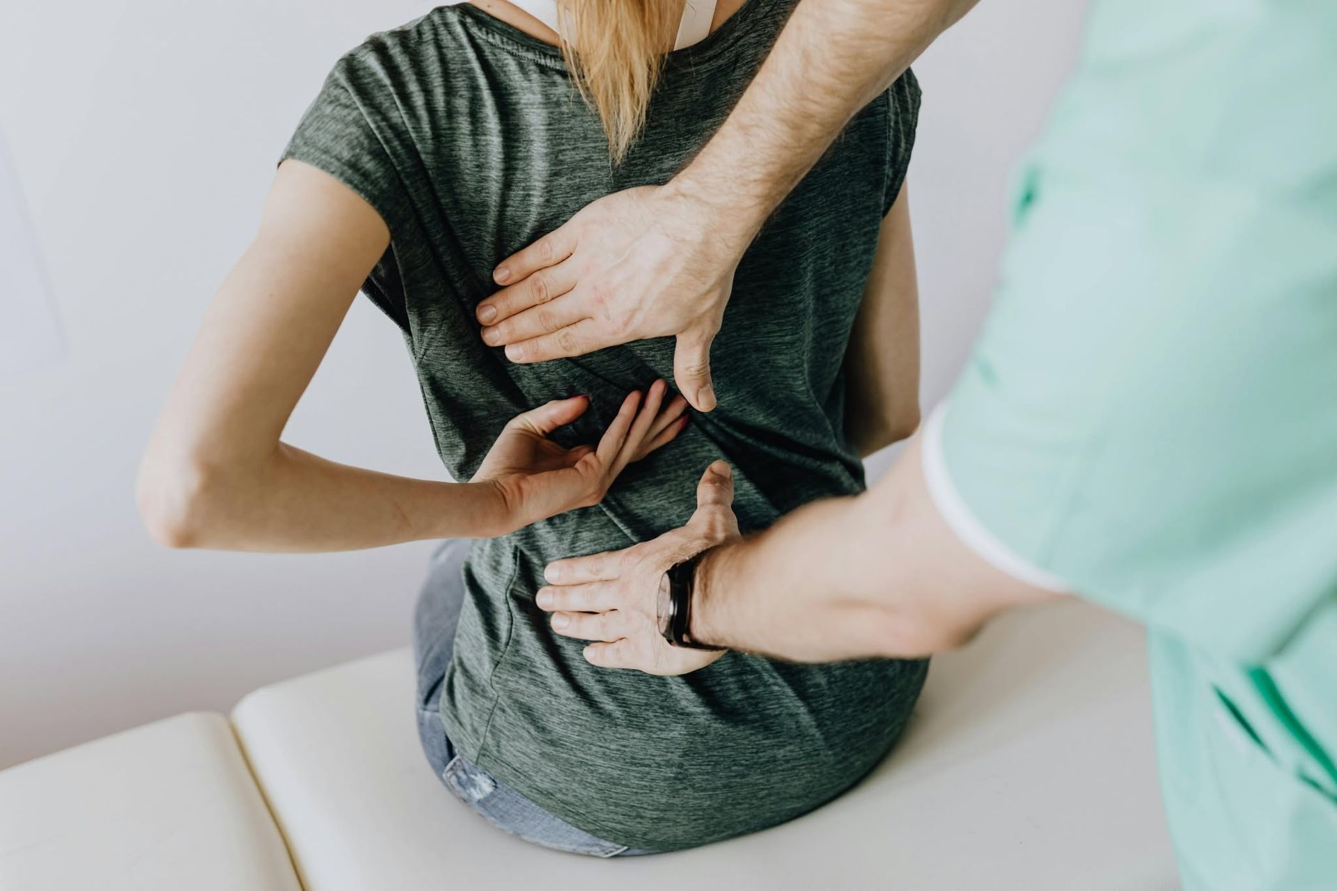 Two people apply a back adjustment to a seated person in a clinic setting