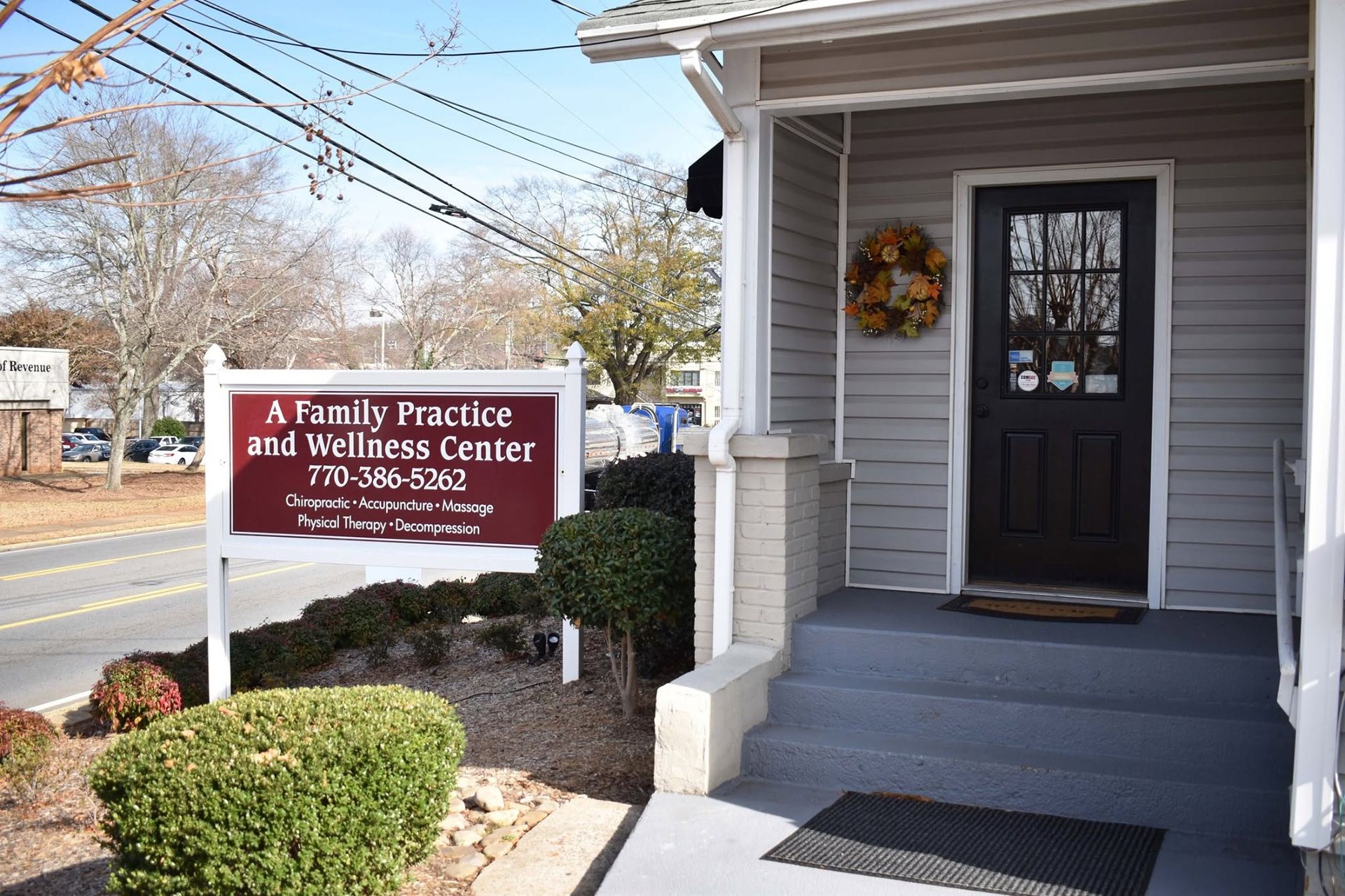 Family Practice and Wellness Center sign beside a gray clinic entrance with a wreath on the door