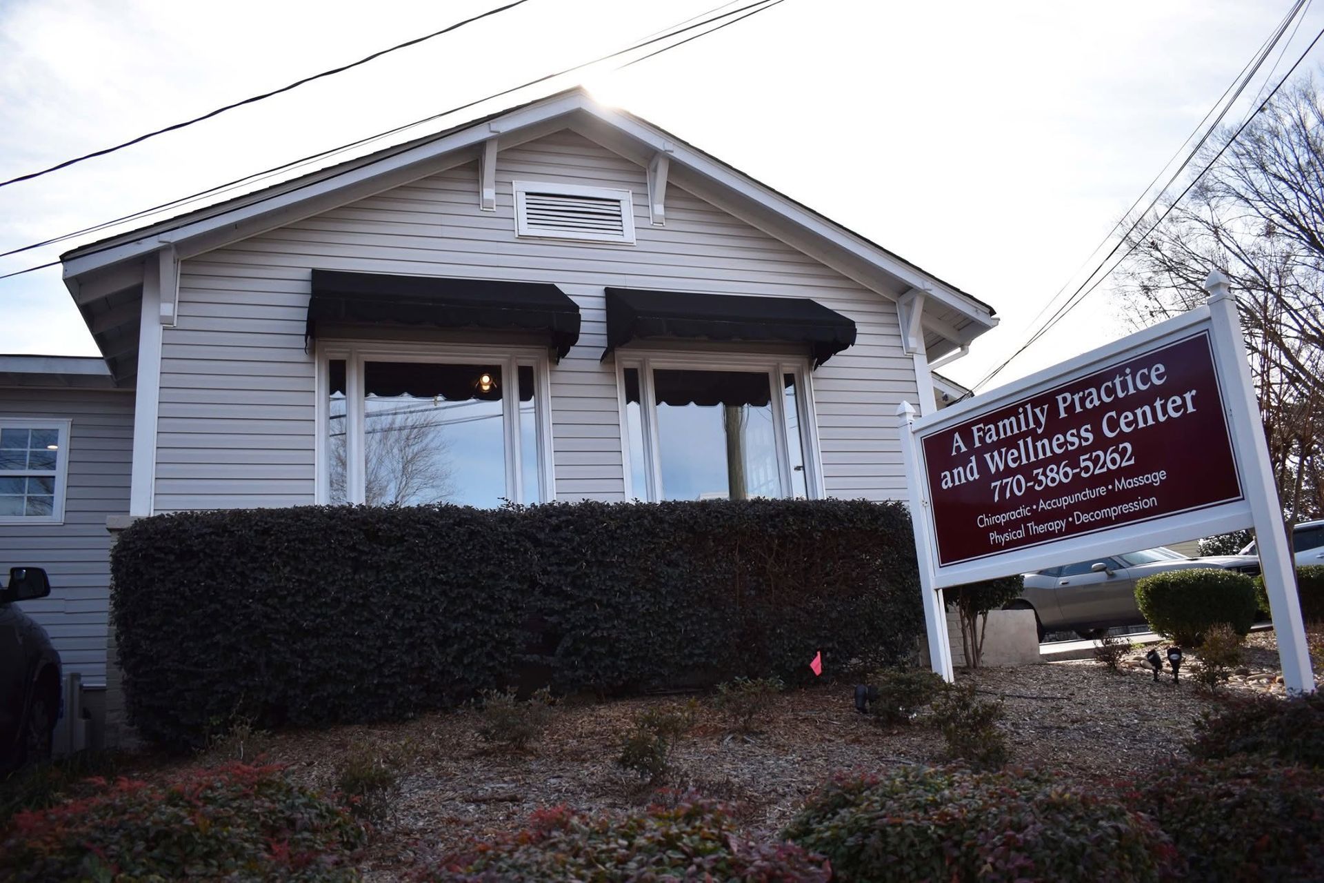 Small house with a hedge and a sign for a practice center in front.