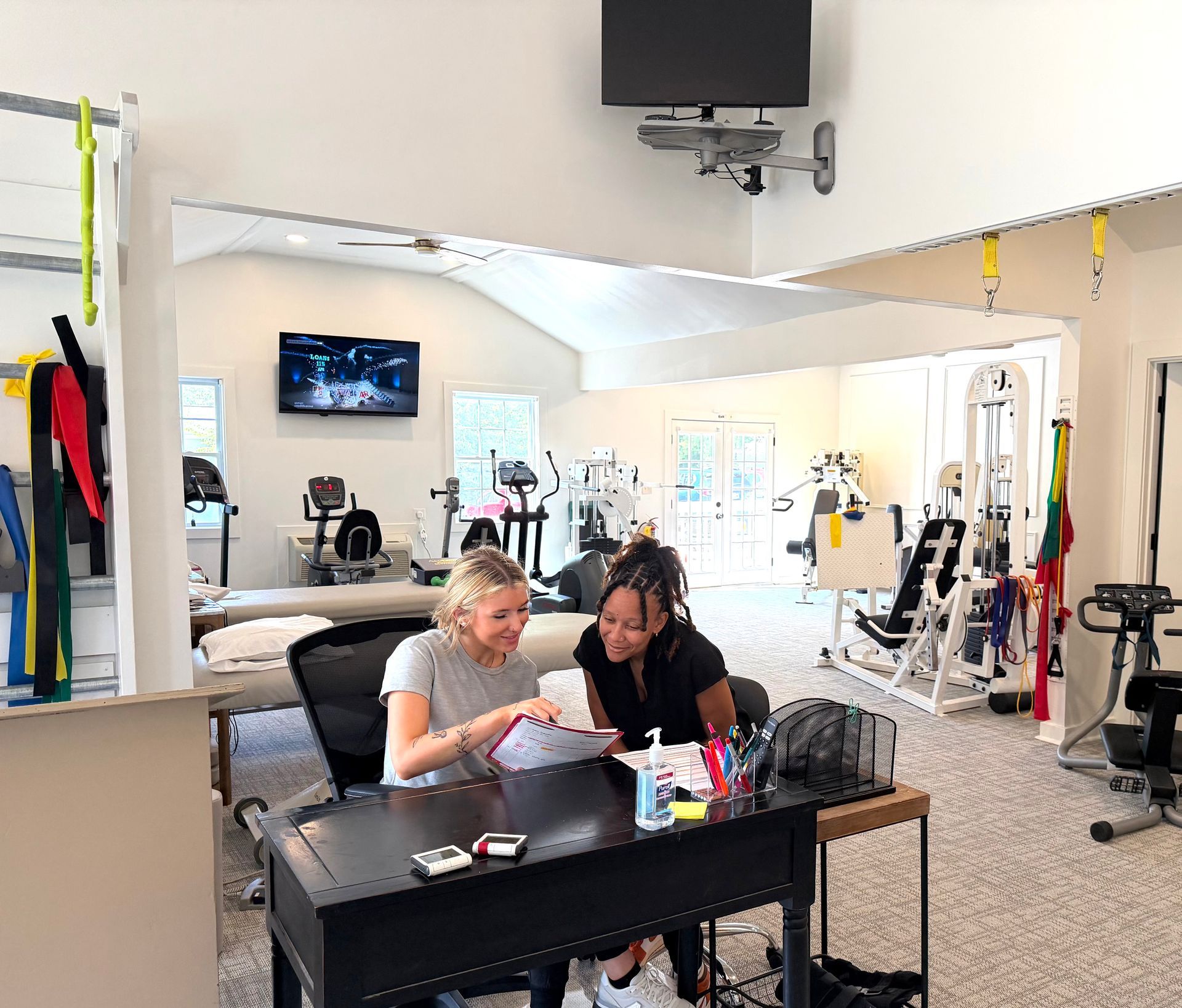 Two people reviewing papers at a desk in a bright physical therapy clinic