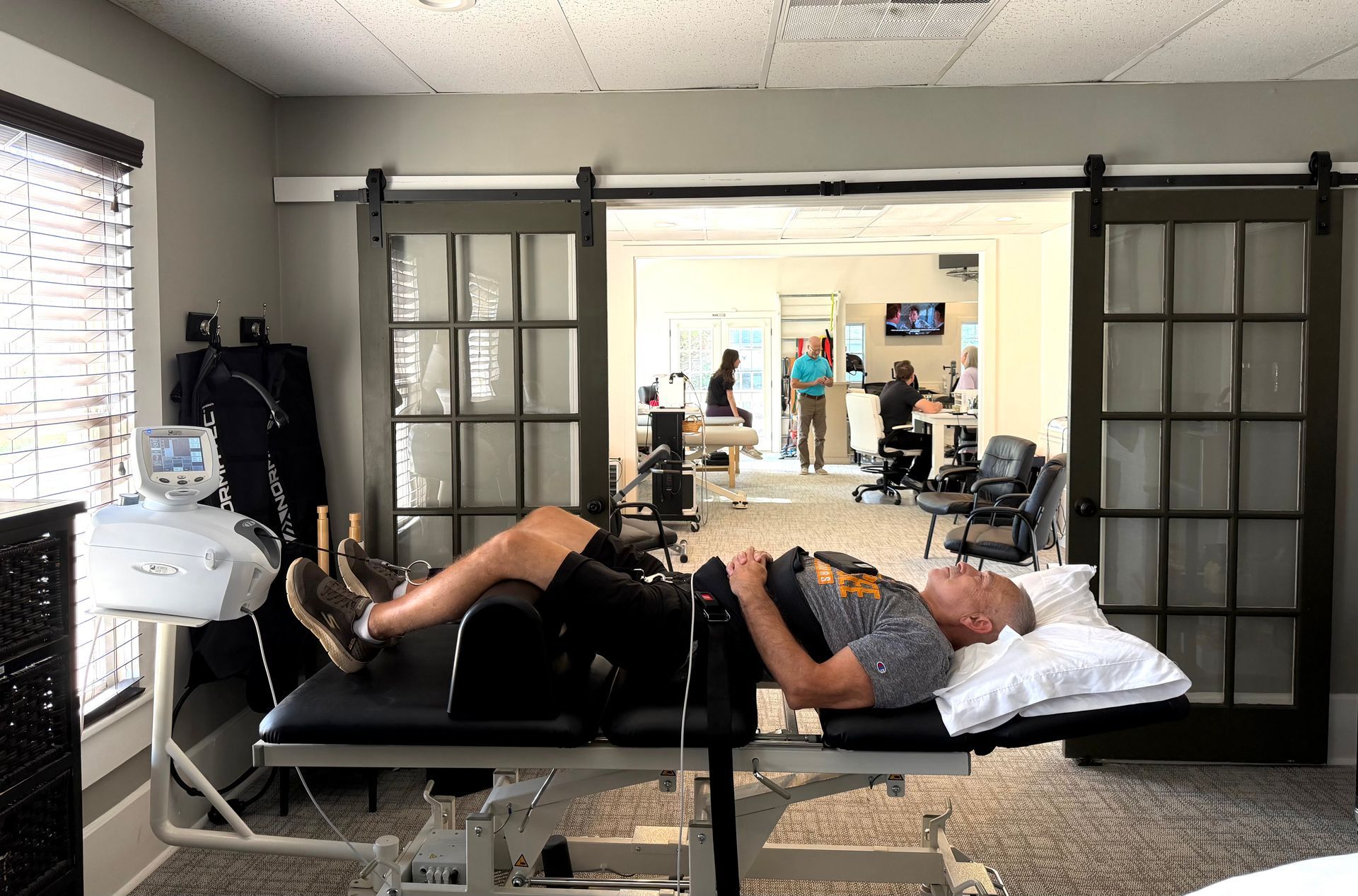 Person lying on a treatment table in a bright studio, with mirrors and exercise equipment in the background